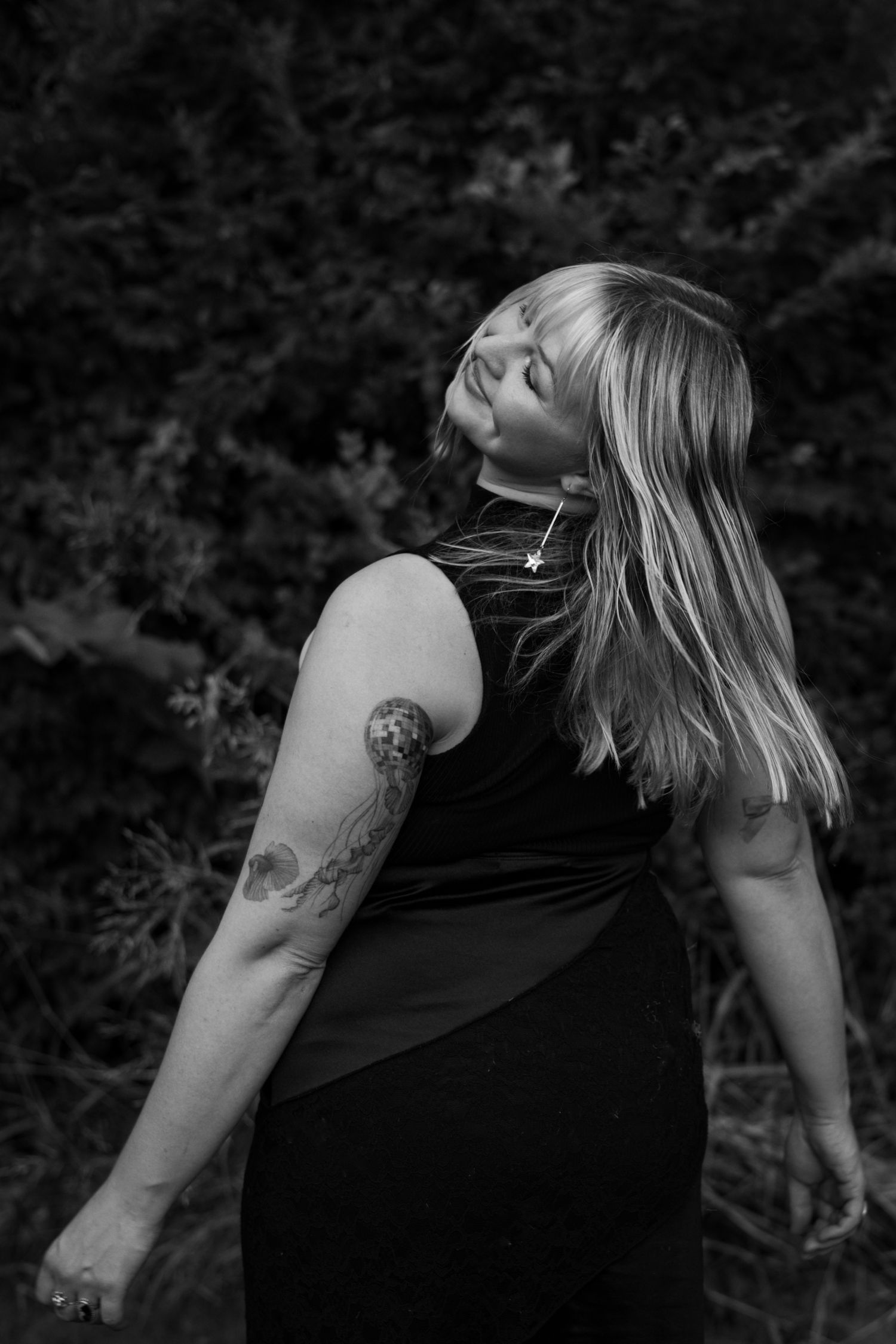 Artistic black and white portrait showing person with tattoo in profile against dark background.