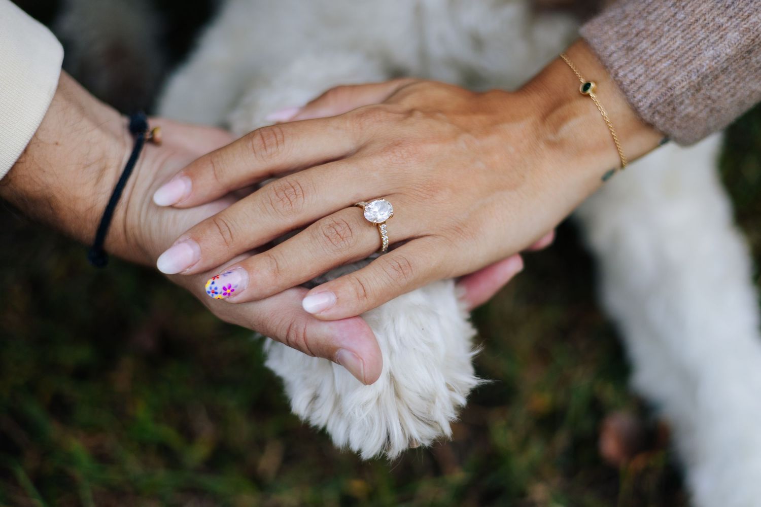 Close-up of hands with engagement ring and interlocked fingers against a soft background.