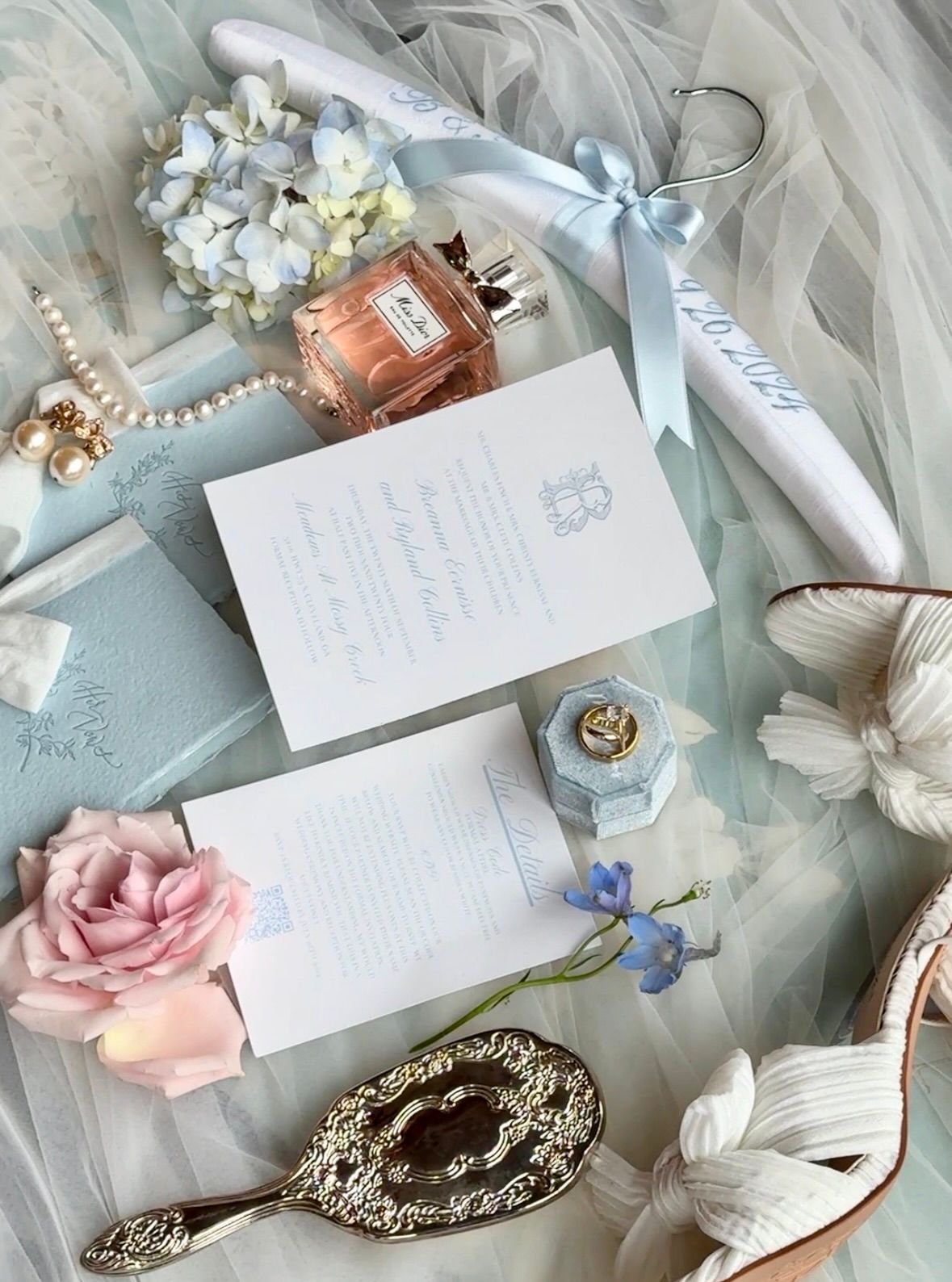 Delicate wedding details including handwritten notes, pink roses, and vintage accessories arranged on soft tulle fabric.