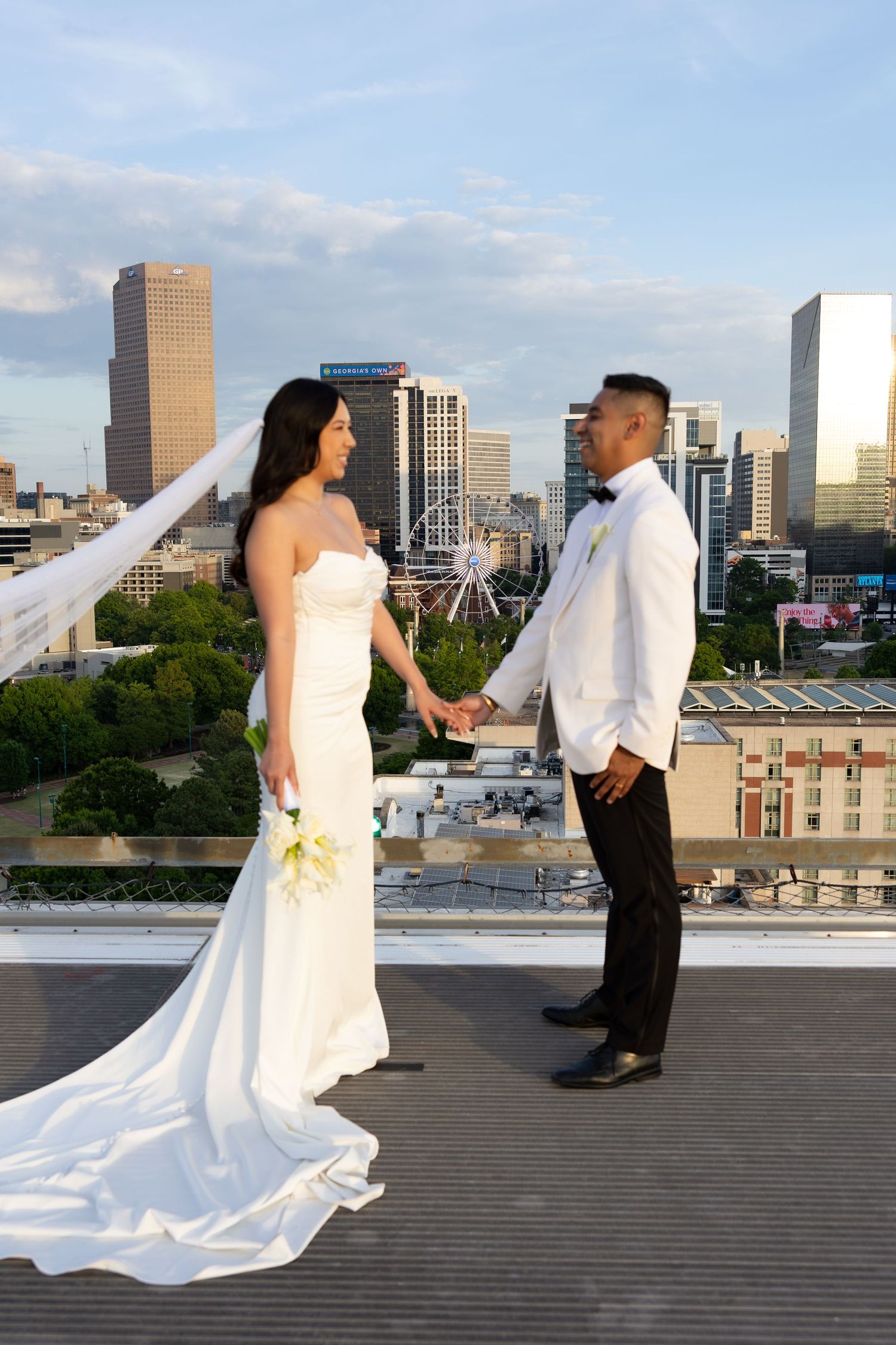Bride and groom holding hands on rooftop with Atlanta city skyline at sunset.