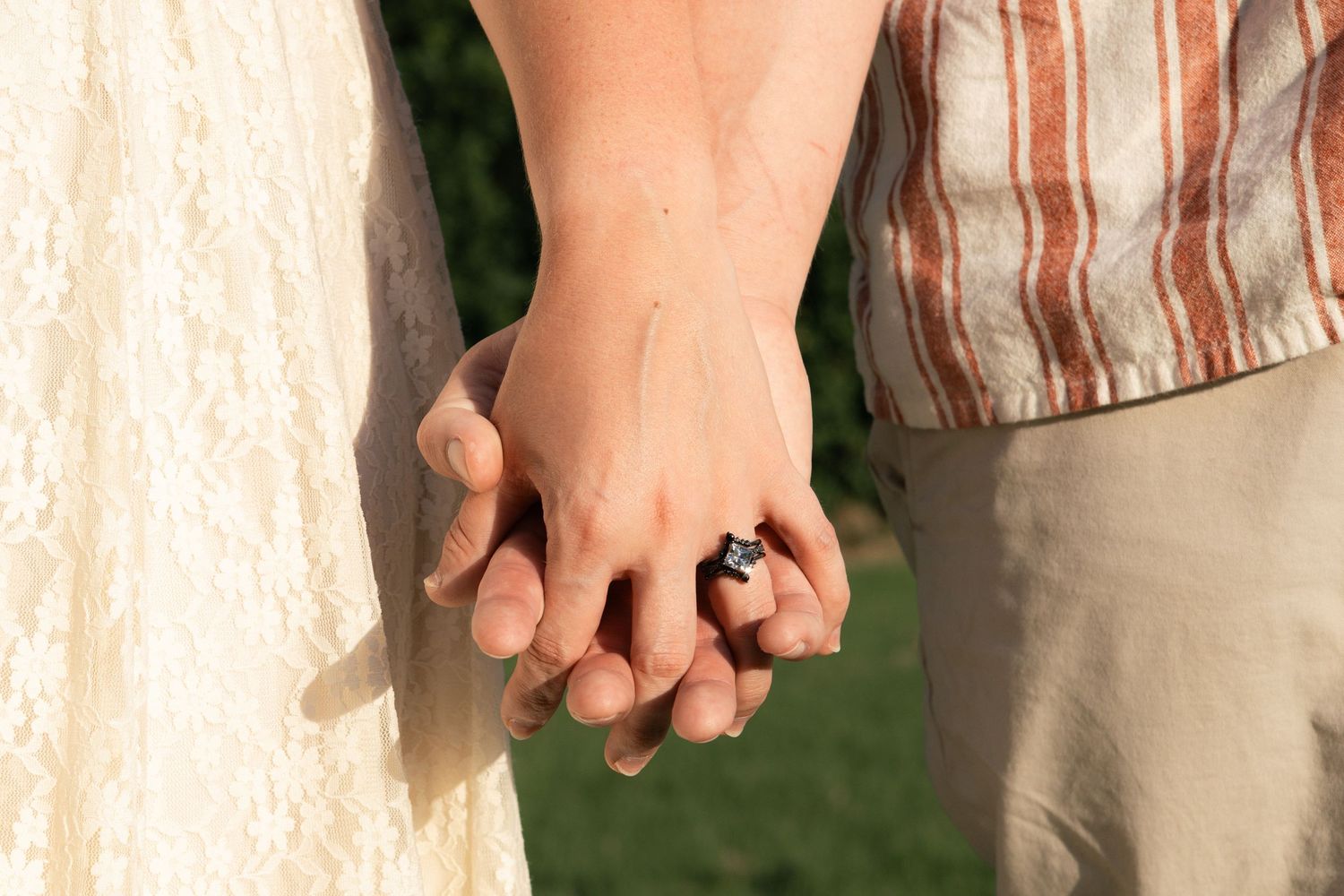 Close-up shot of two people holding hands outdoors in natural lighting.