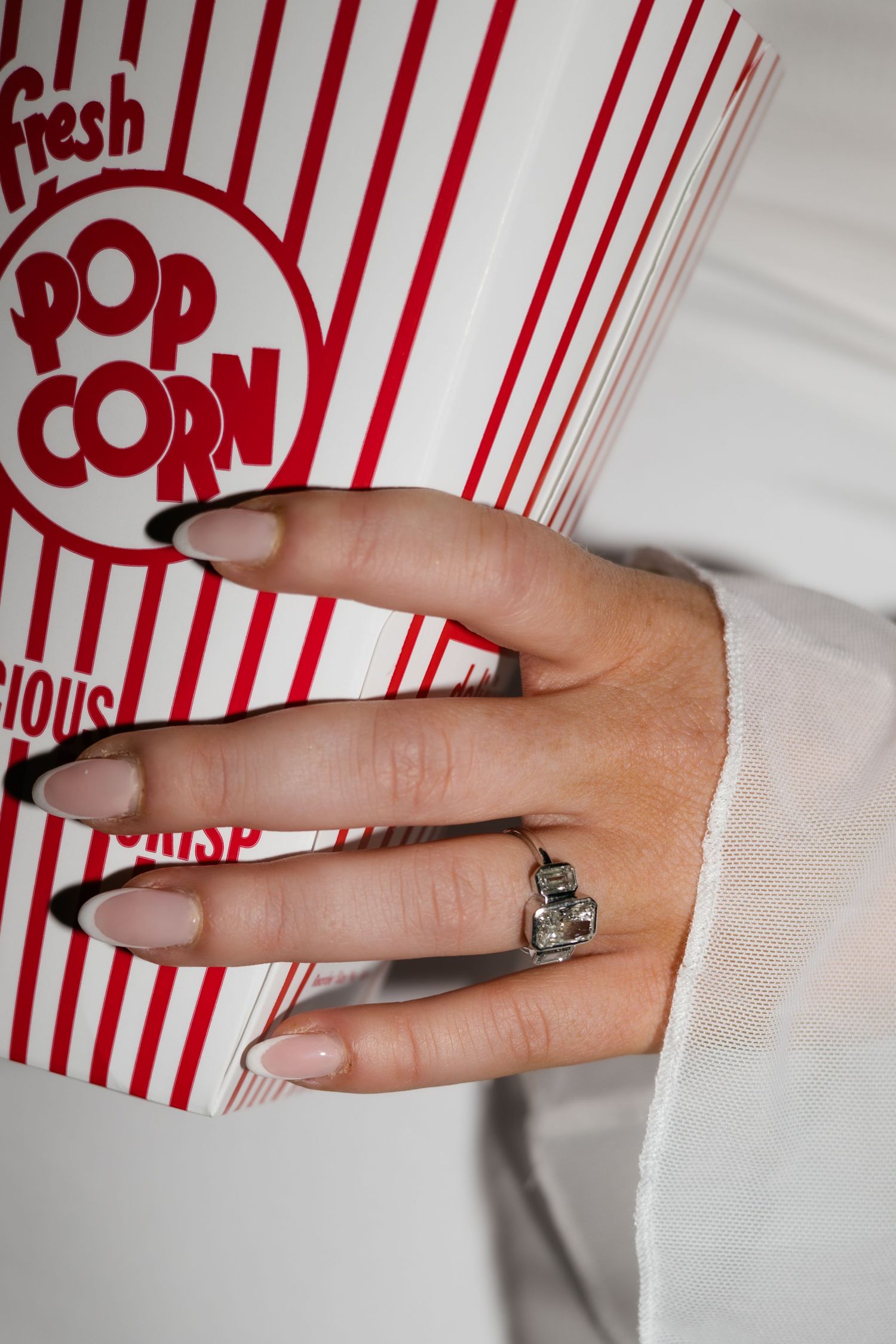 A hand wearing a diamond ring holds a classic striped popcorn container.
