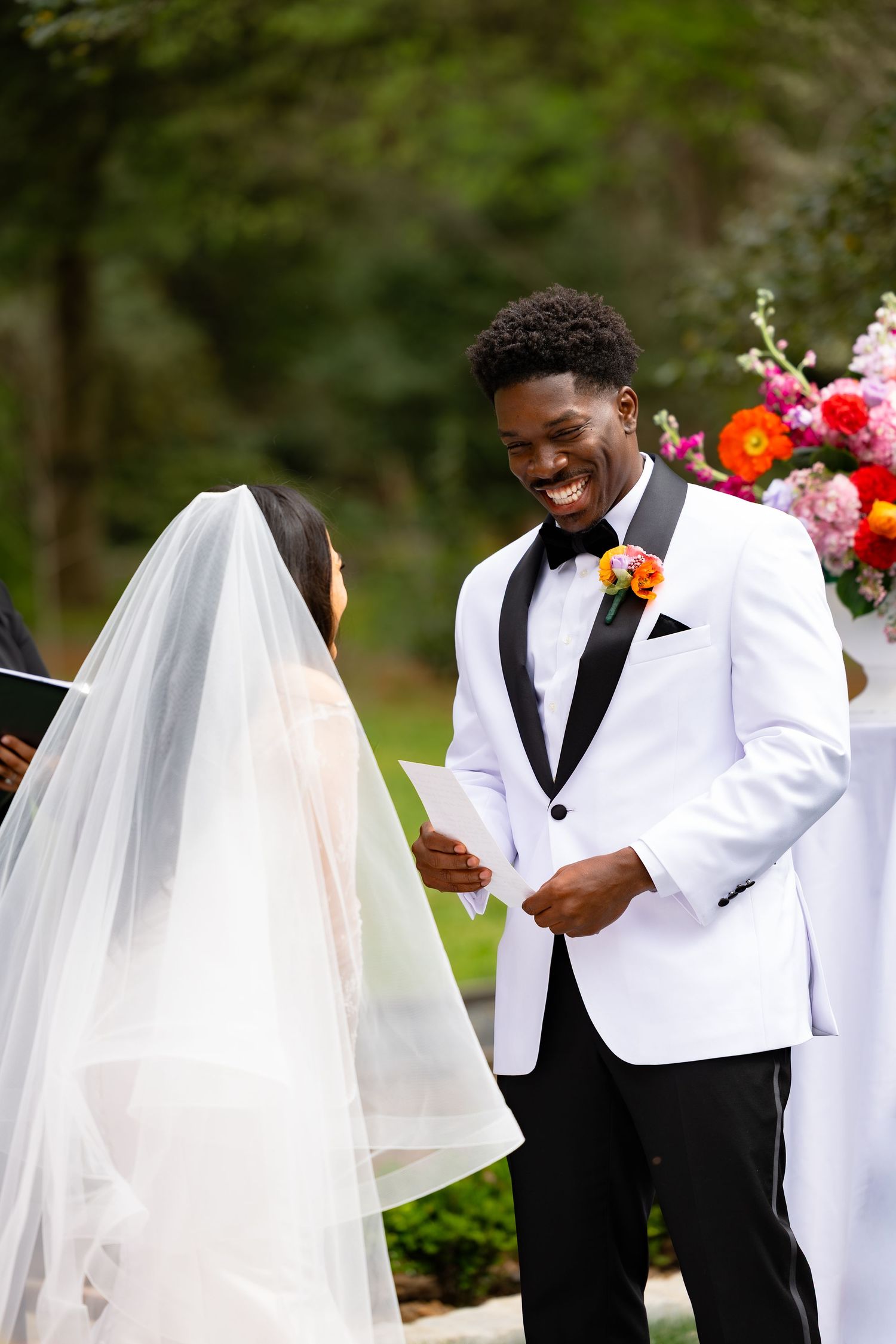 Wedding party members in white tuxedos share joyful moments and laughter during outdoor photo session.