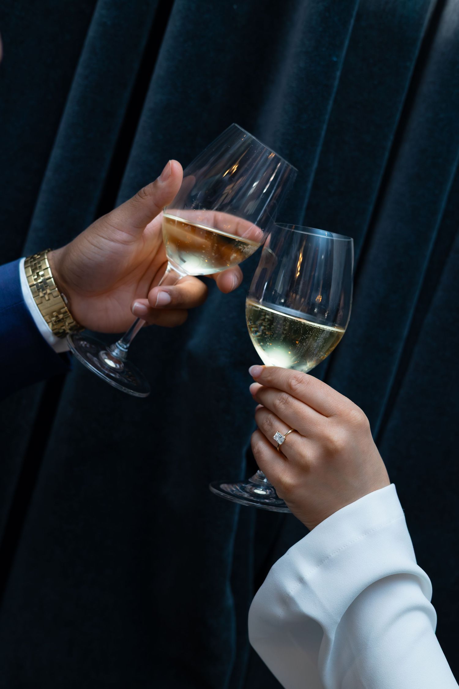 Hand in white sleeve holding a wine glass with light colored wine against dark background.