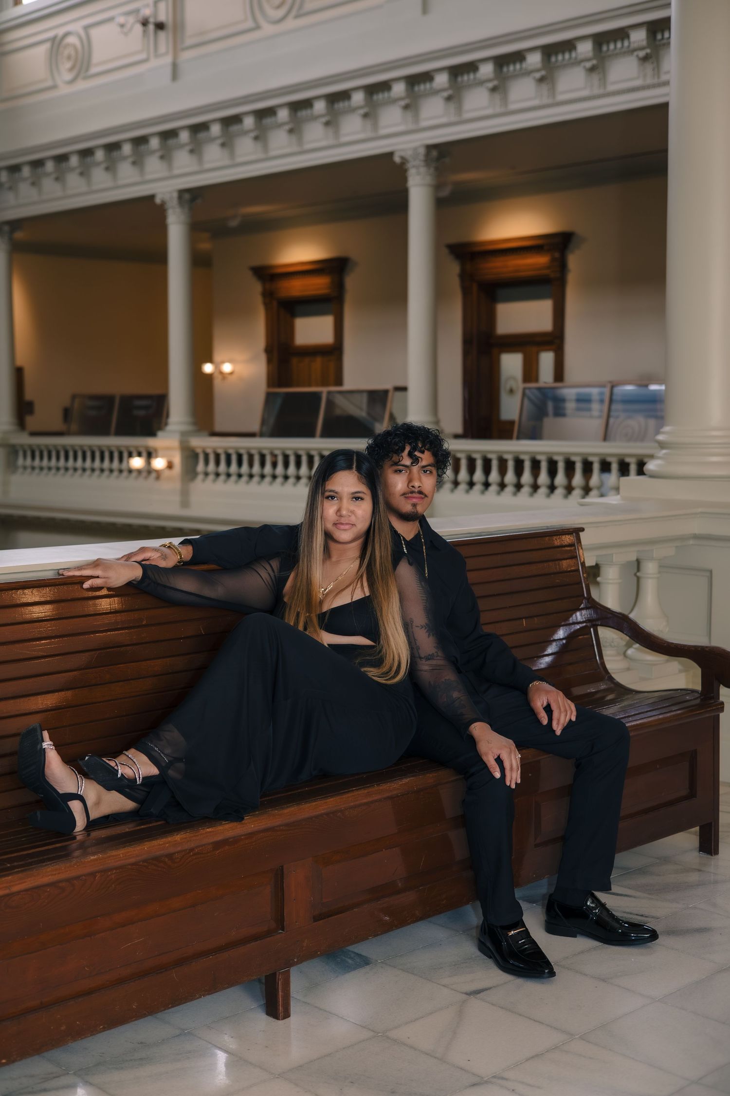 Couple relaxes on wooden church pews in a historic building with columns and ornate details.