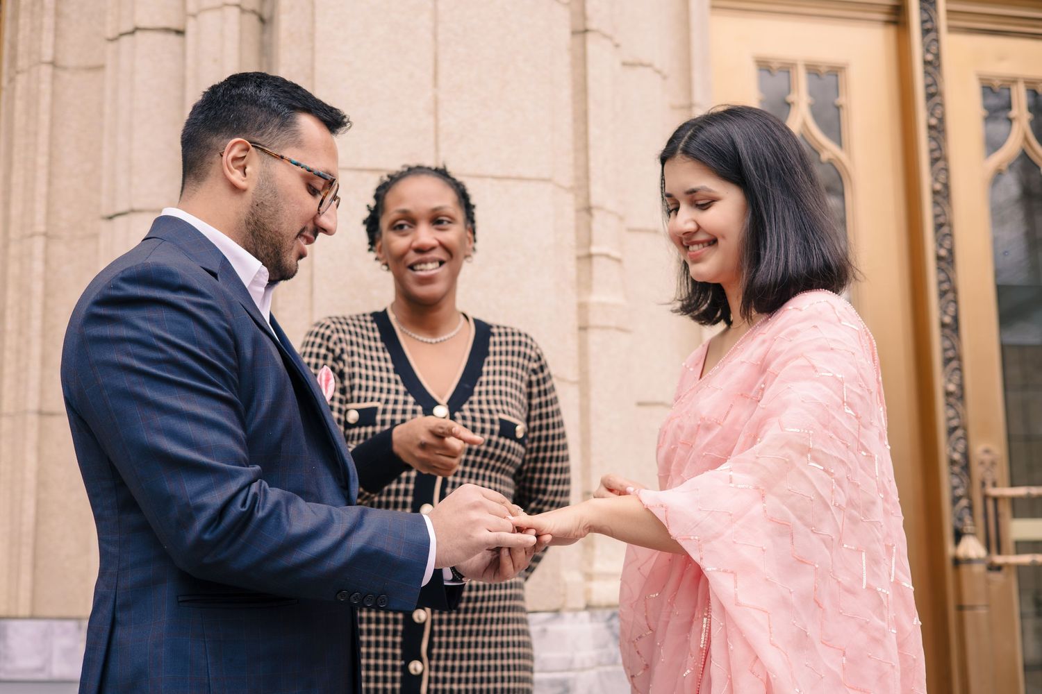 A civil ceremony takes place outside a historic building with three people in formal attire.