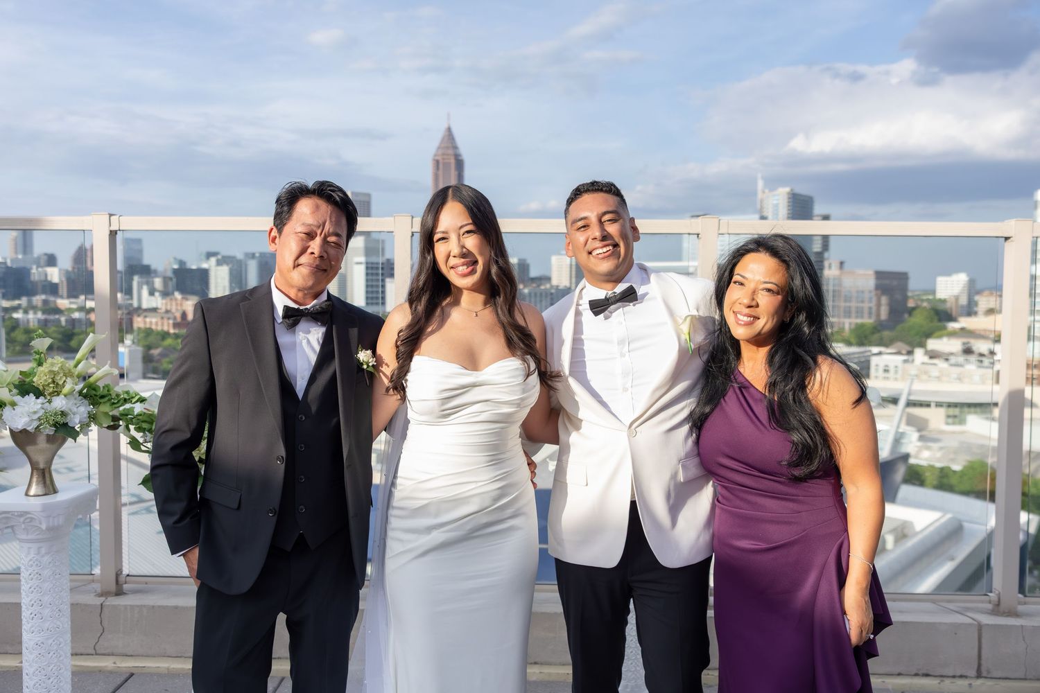Wedding couple with family posing on rooftop with city skyline backdrop.