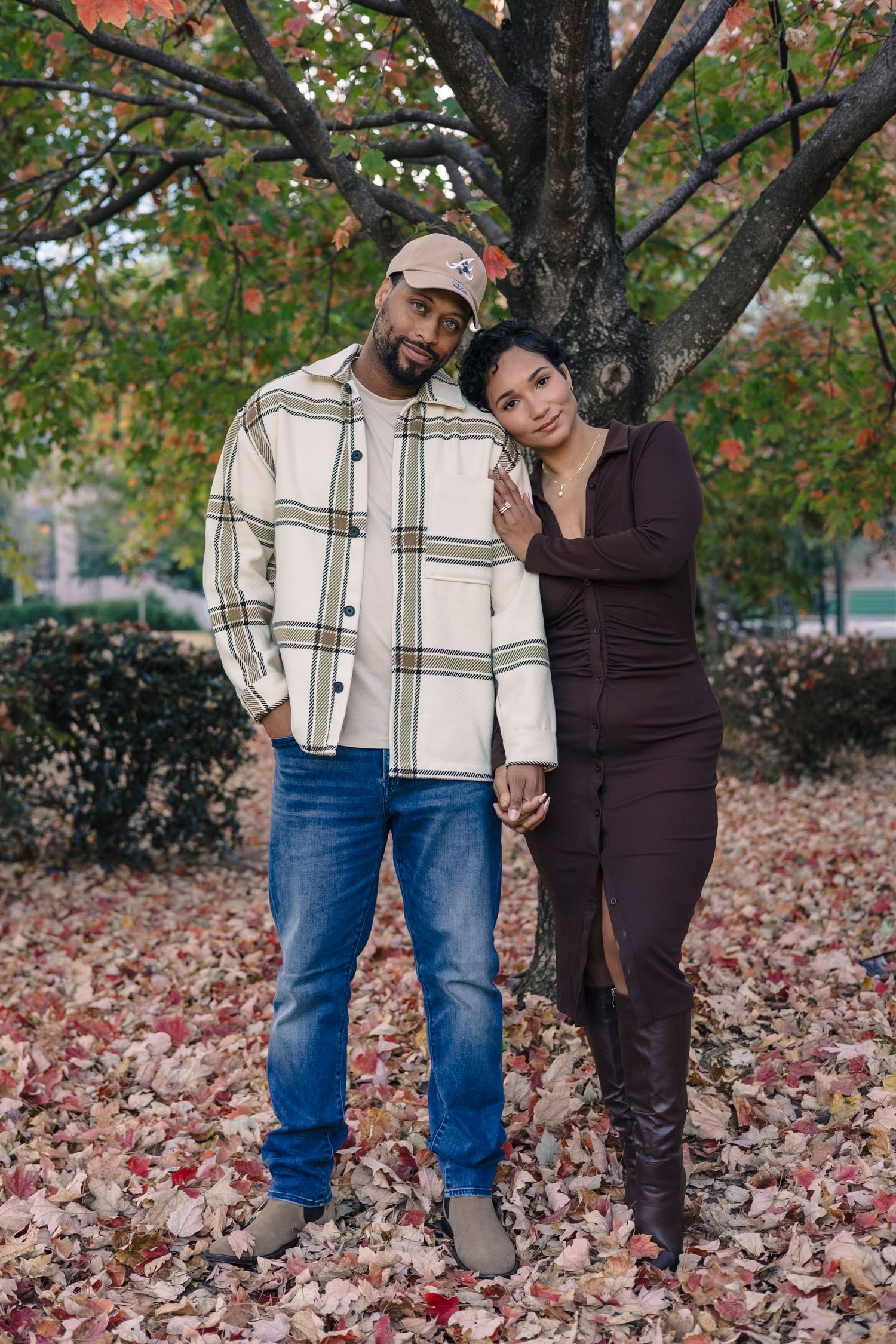 A couple enjoys playful moments together among fallen autumn leaves under a tree.