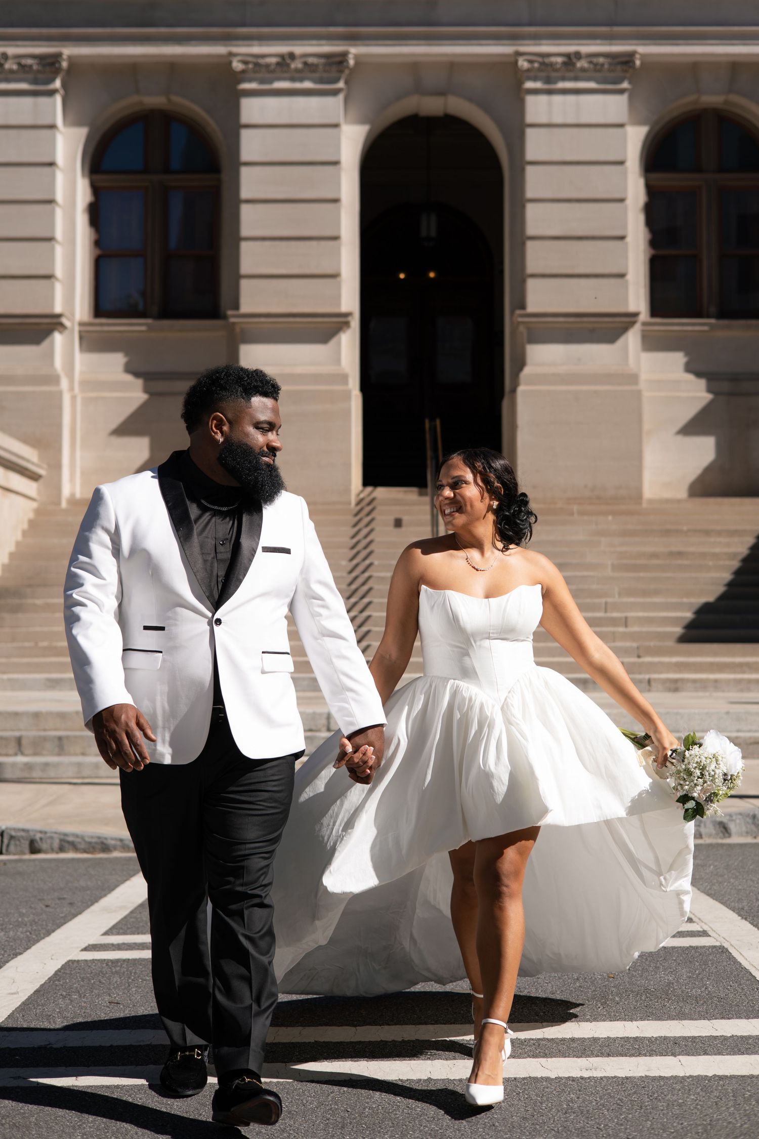 A bride and groom in formal attire pose dramatically on urban steps.