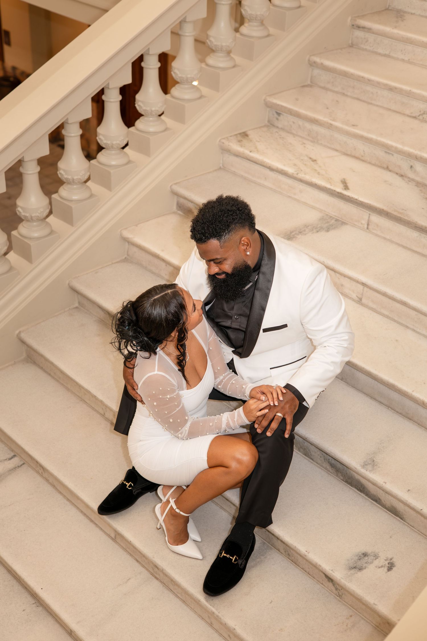 Romantic couple in formal attire posing on grand white marble steps.