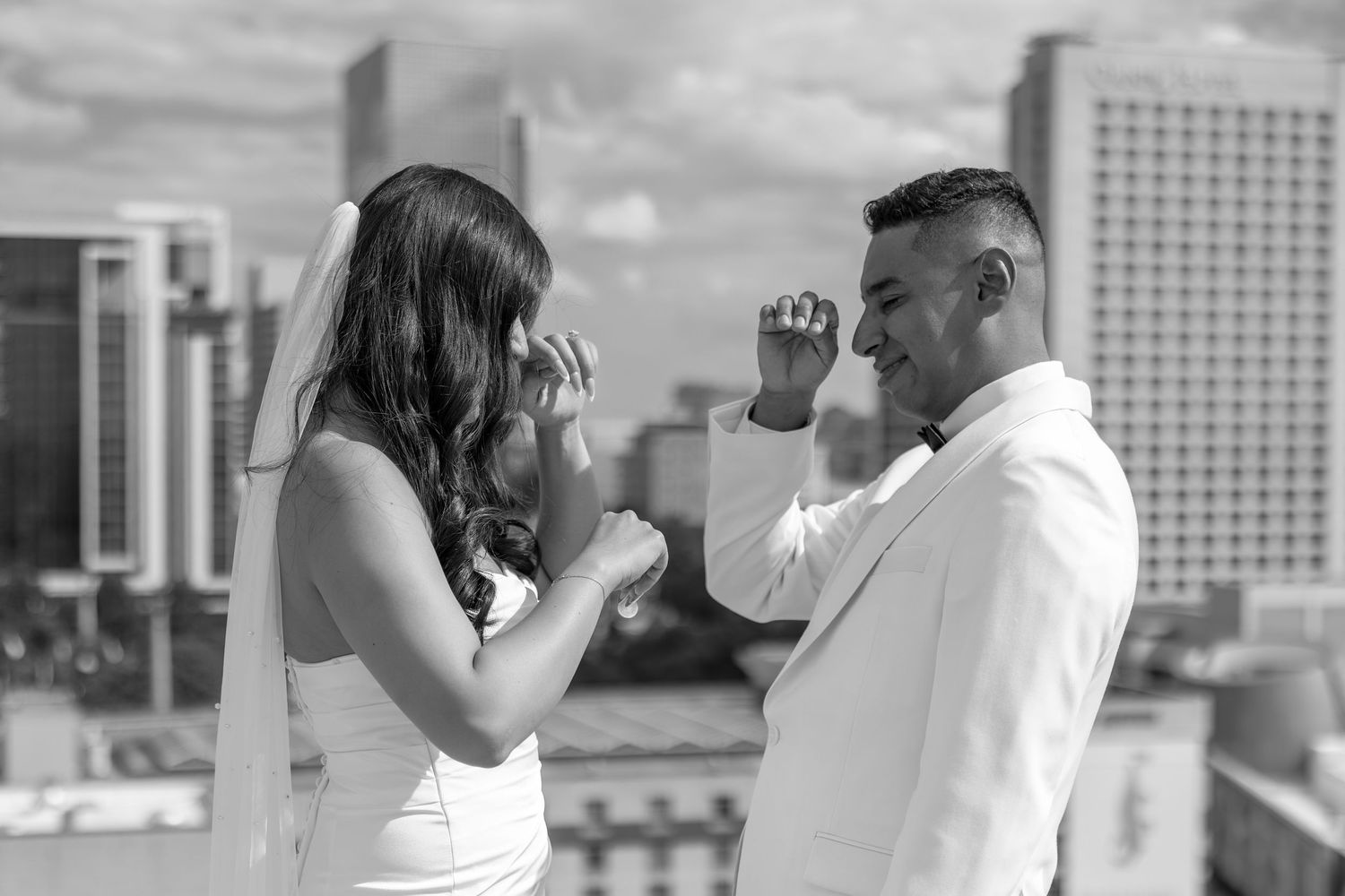 Black and white photo of a bride and groom sharing a toast on a rooftop with city skyline backdrop.