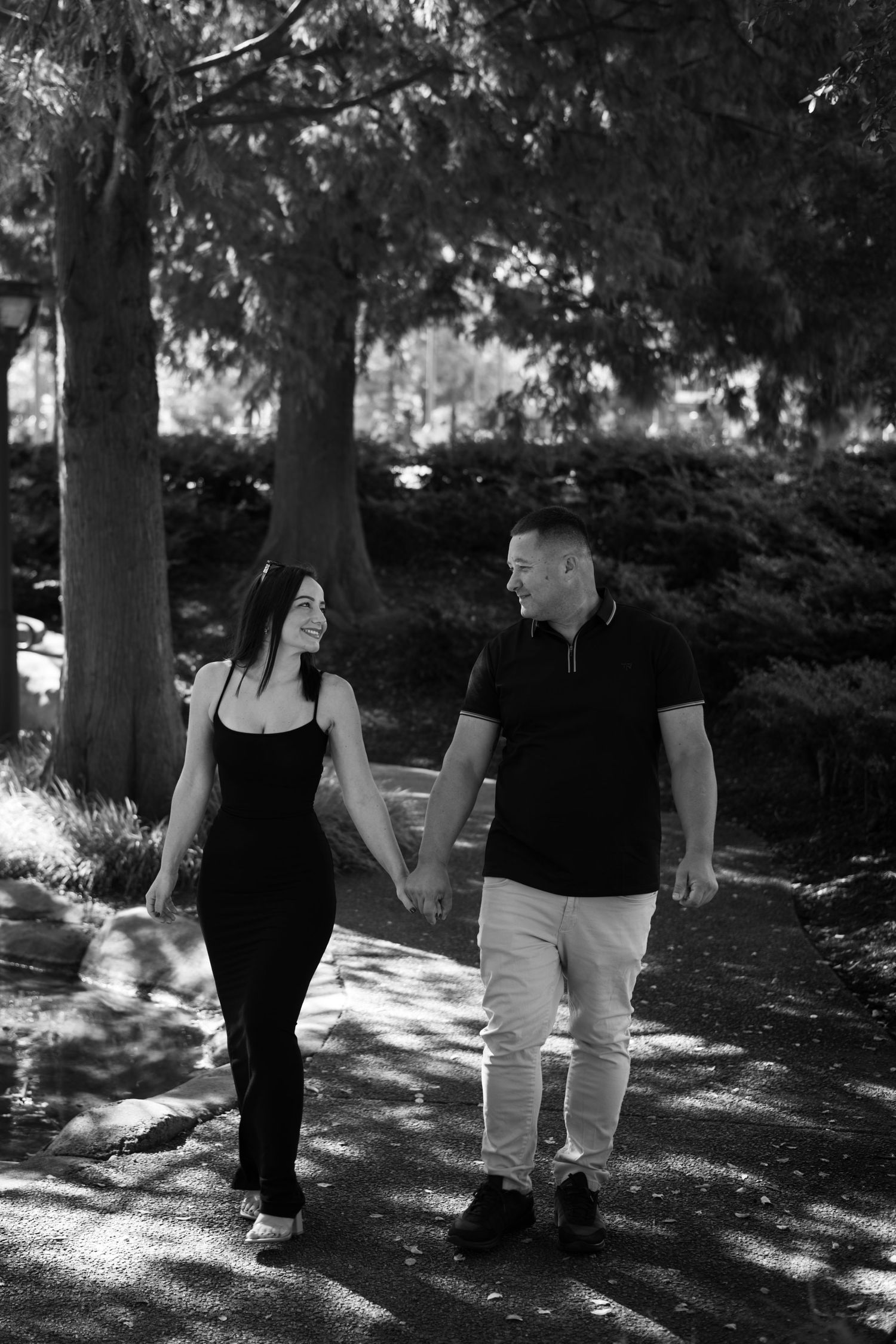 Black and white photo of couple walking together through a tree-lined path.