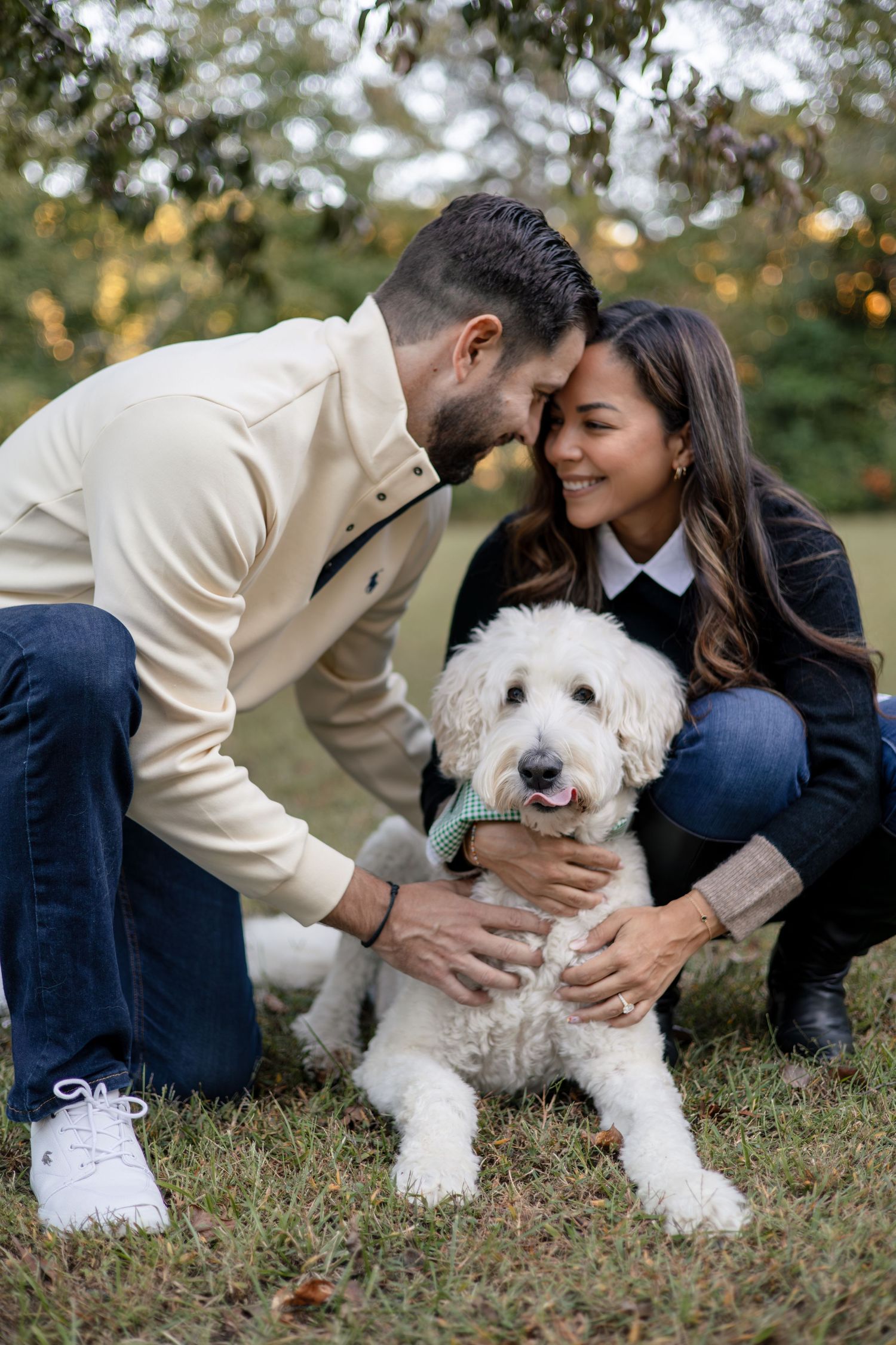 Couple playing with white fluffy dog on grass during autumn photoshoot.
