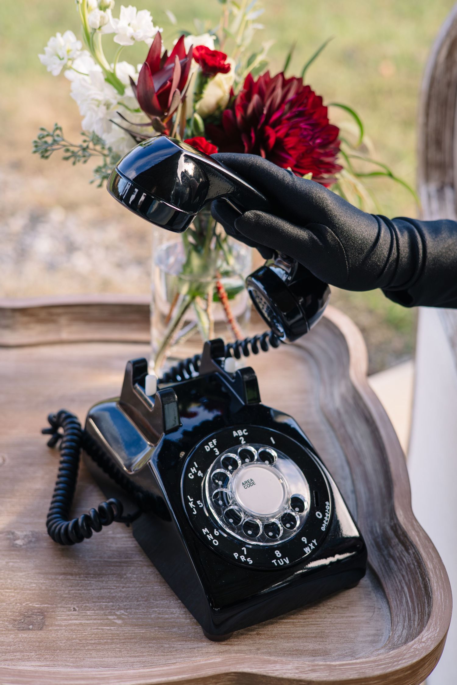 Vintage black rotary phone with red flowers arranged on wooden surface for wedding decor.