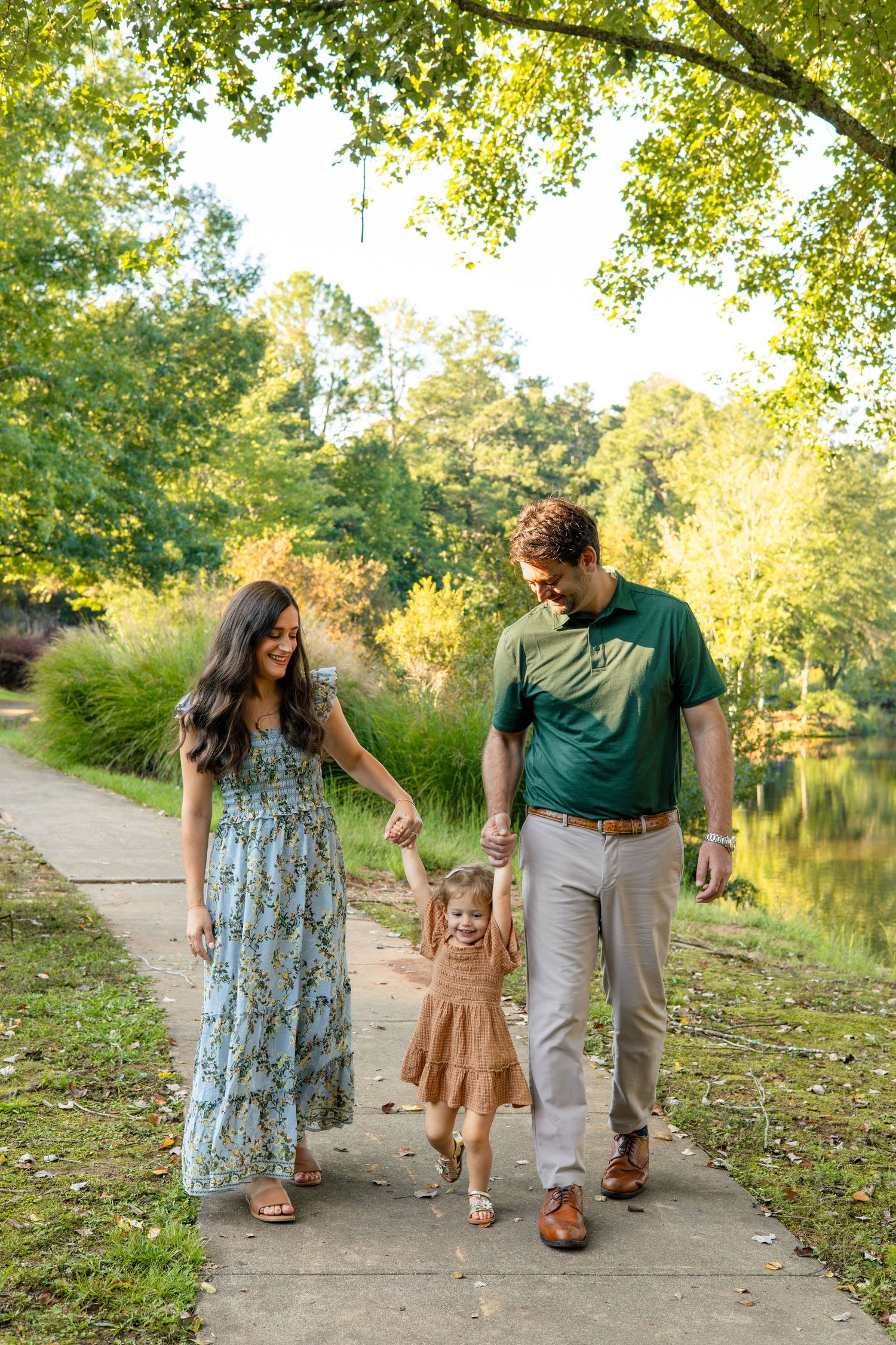 Walking together on a tree-lined path near a peaceful lake on an autumn day.