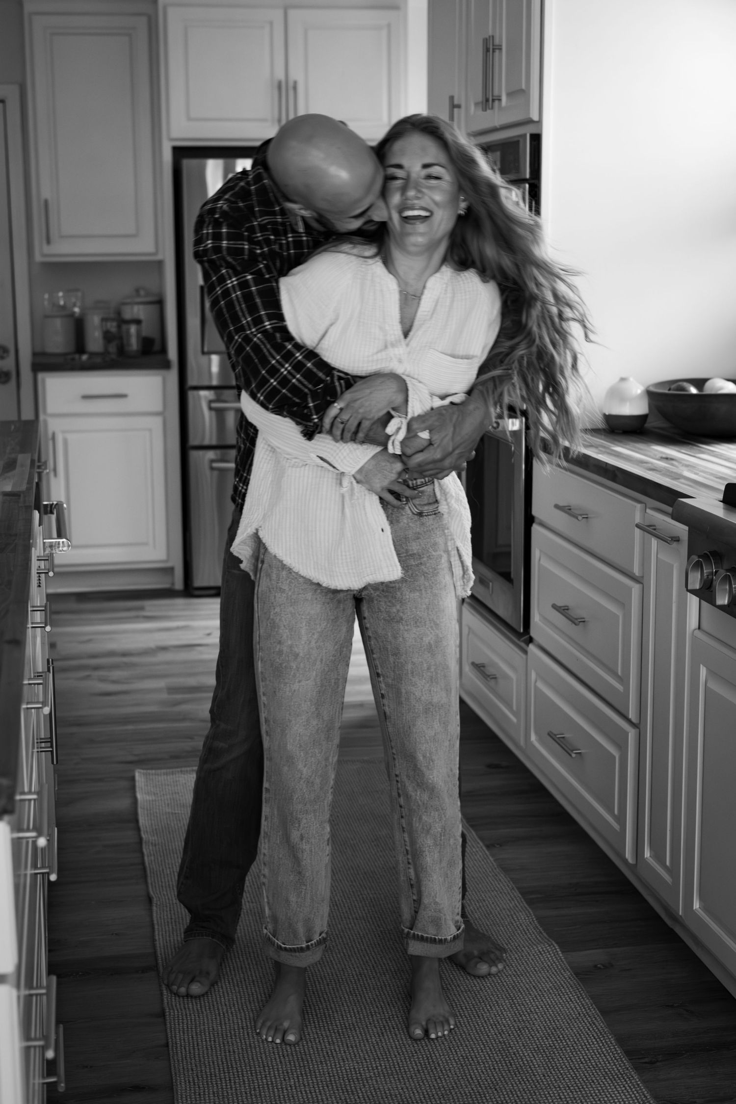 Black and white photos of a couple dancing joyfully in their modern kitchen.