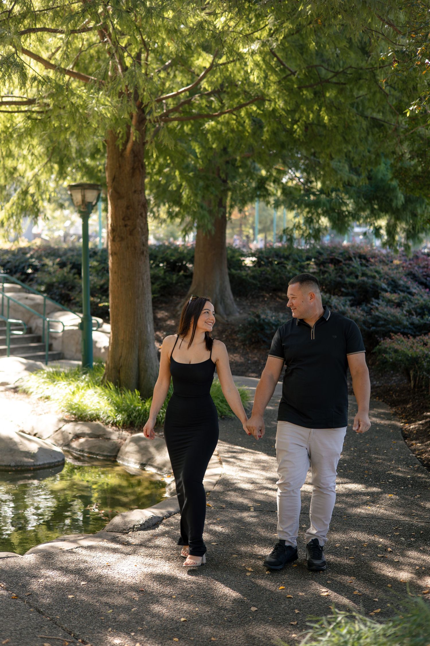 Couple walking together on tree-lined path in sunny park setting.
