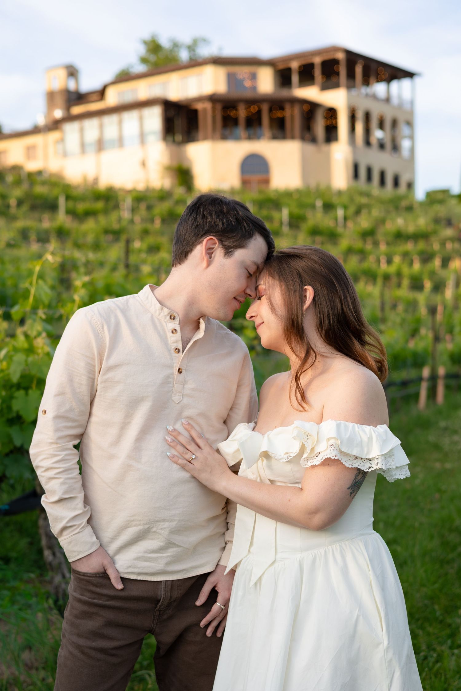 Couple sharing a romantic moment in a vineyard with a winery building in the background.