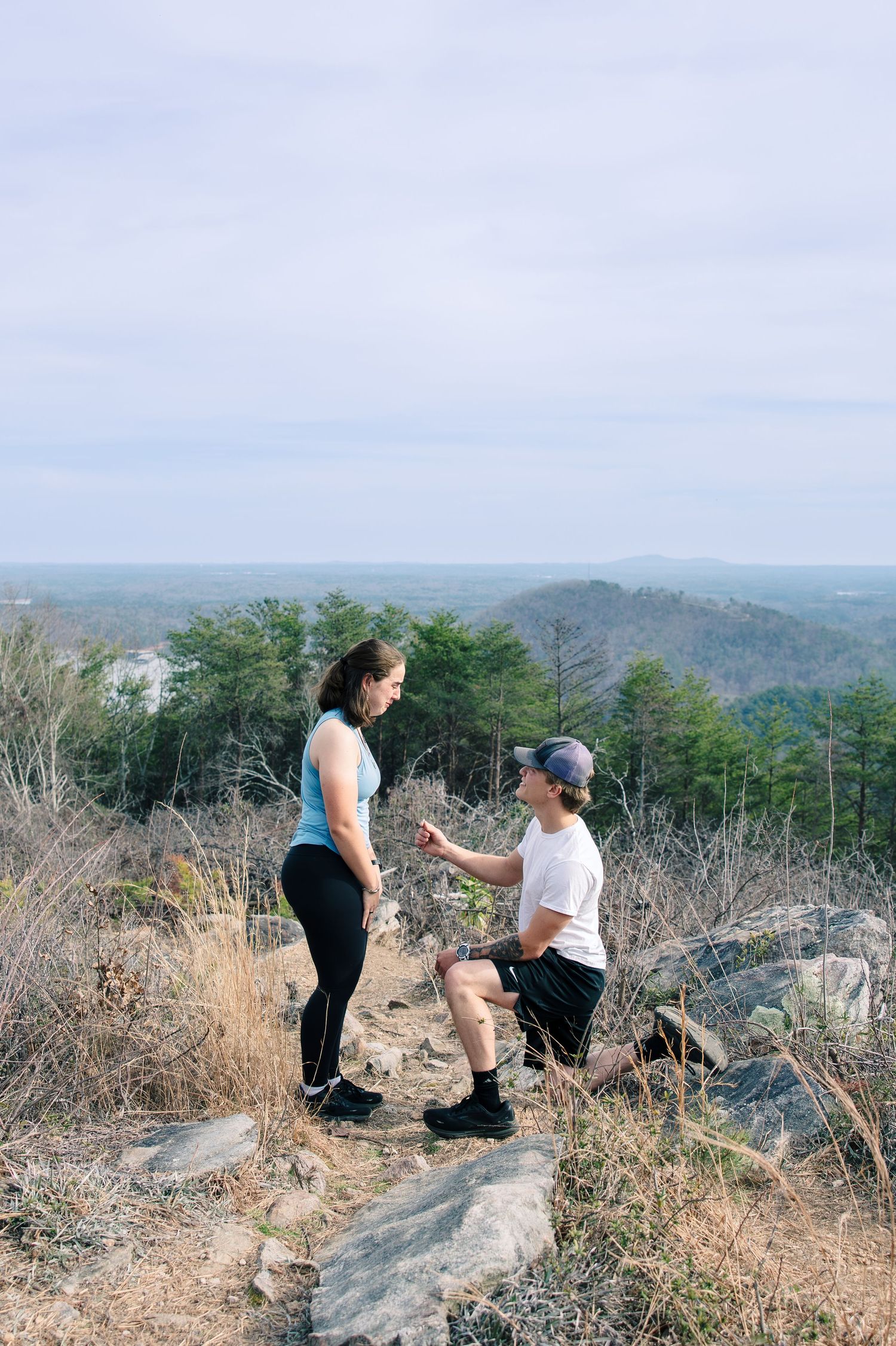 Two people share a special moment during a mountaintop proposal with scenic mountain views in the background.