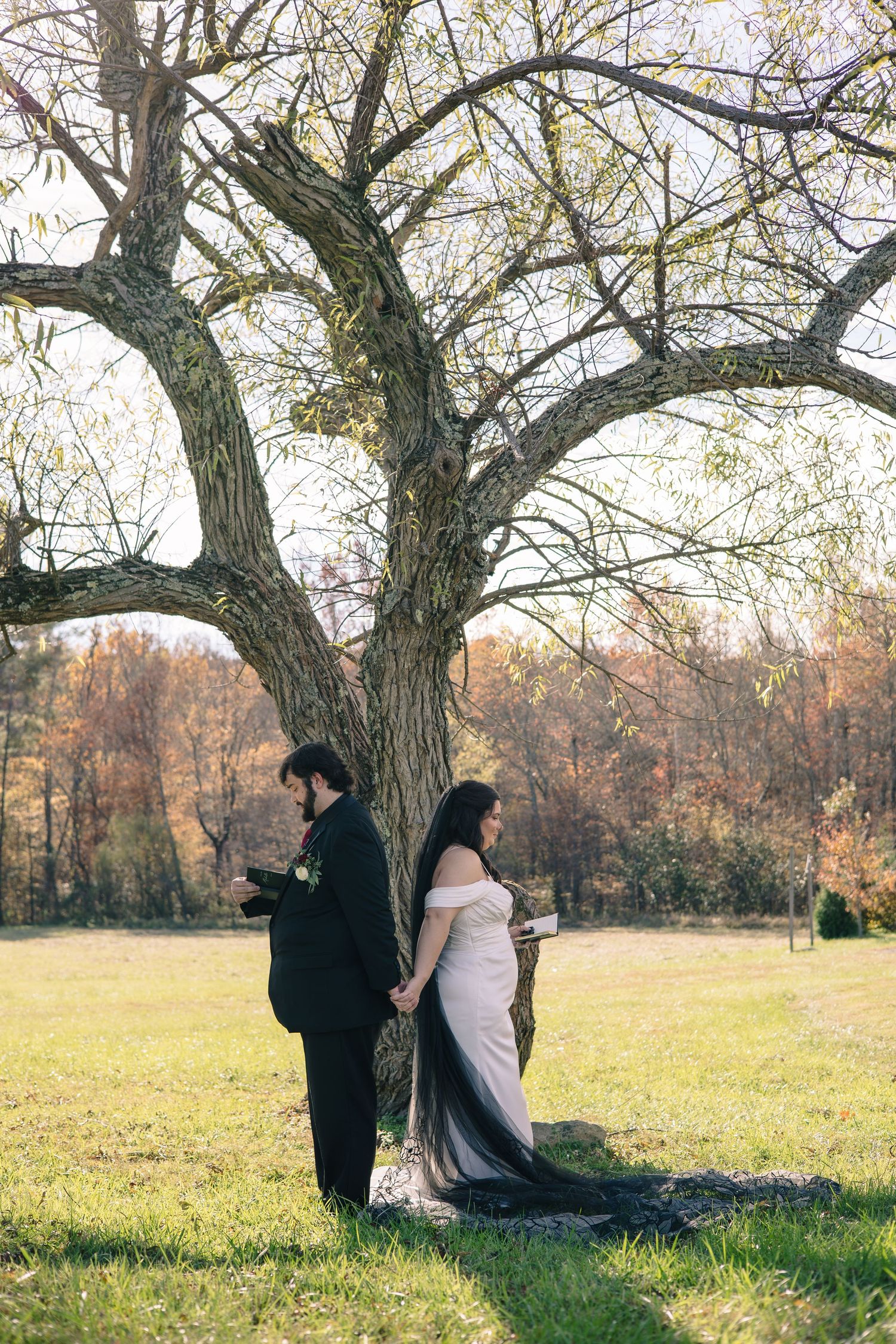 Wedding couple poses under large tree during autumn outdoor photo session.