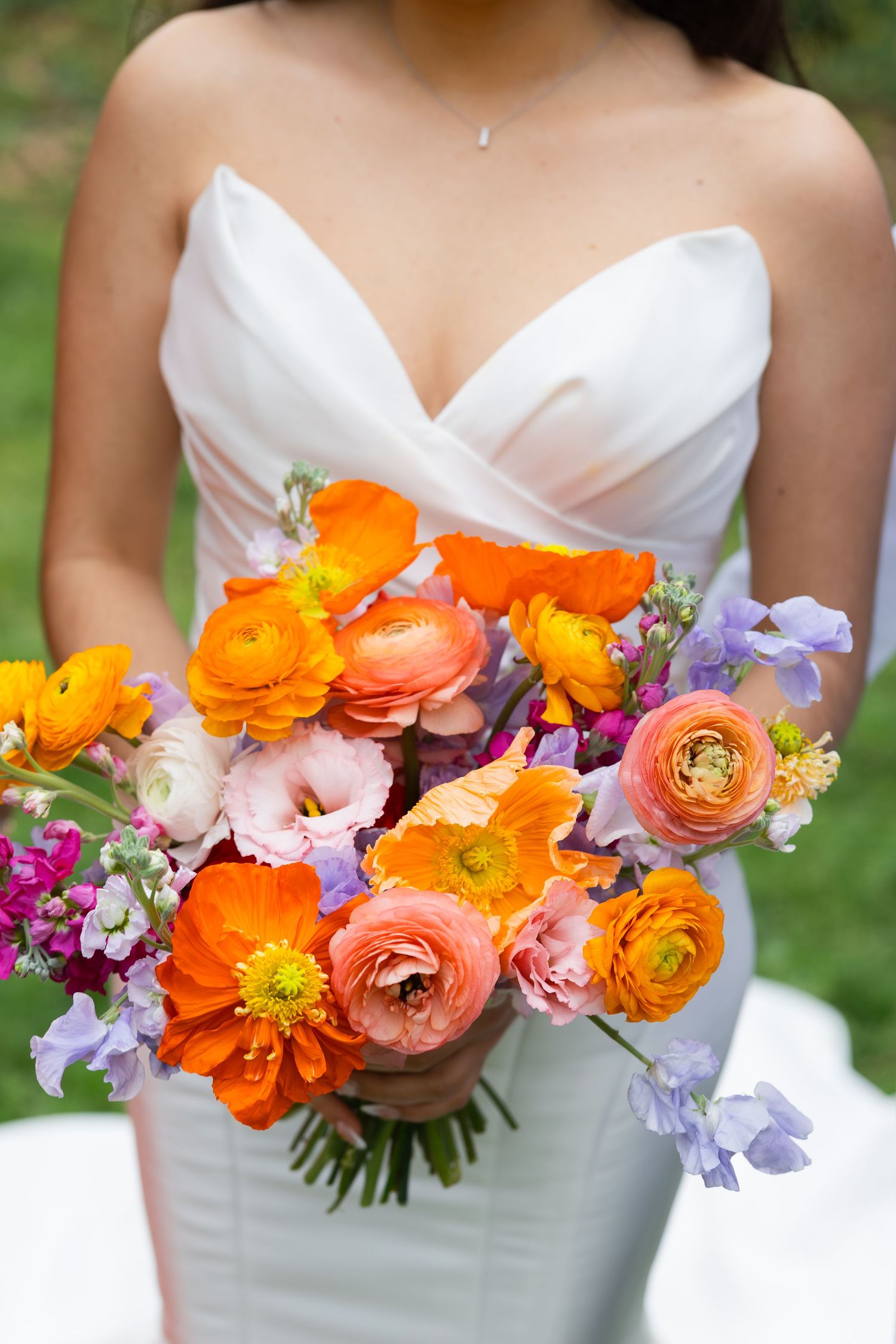 A bouquet of vibrant orange and purple flowers held by a person in a white dress, against a blurred natural background.