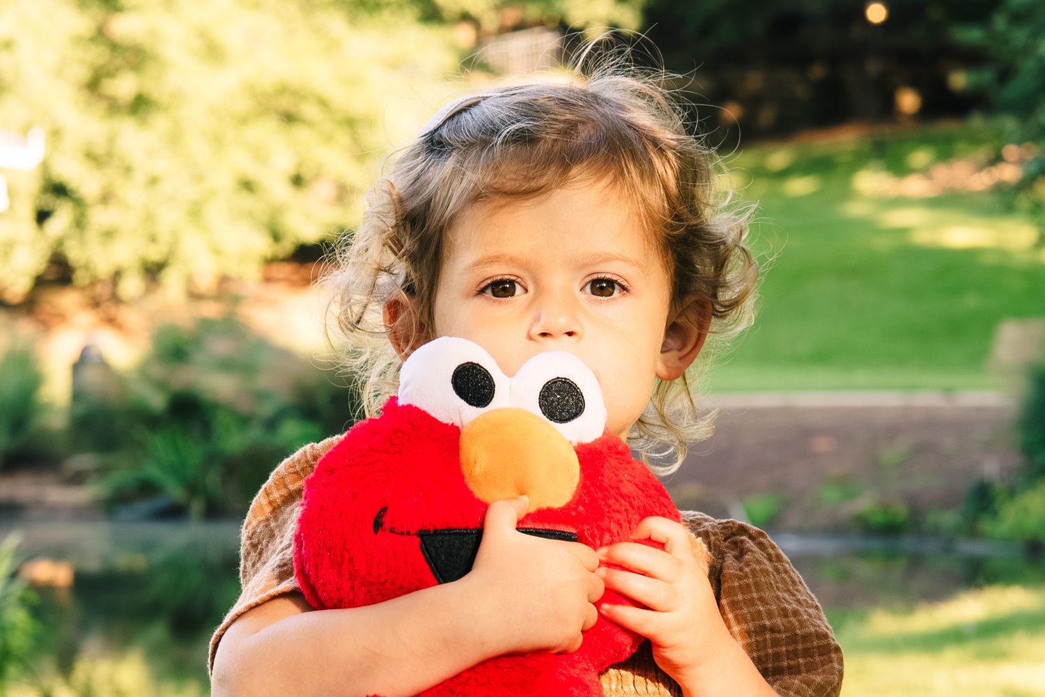 Child playing with red plush toy in warm sunlit outdoor setting.