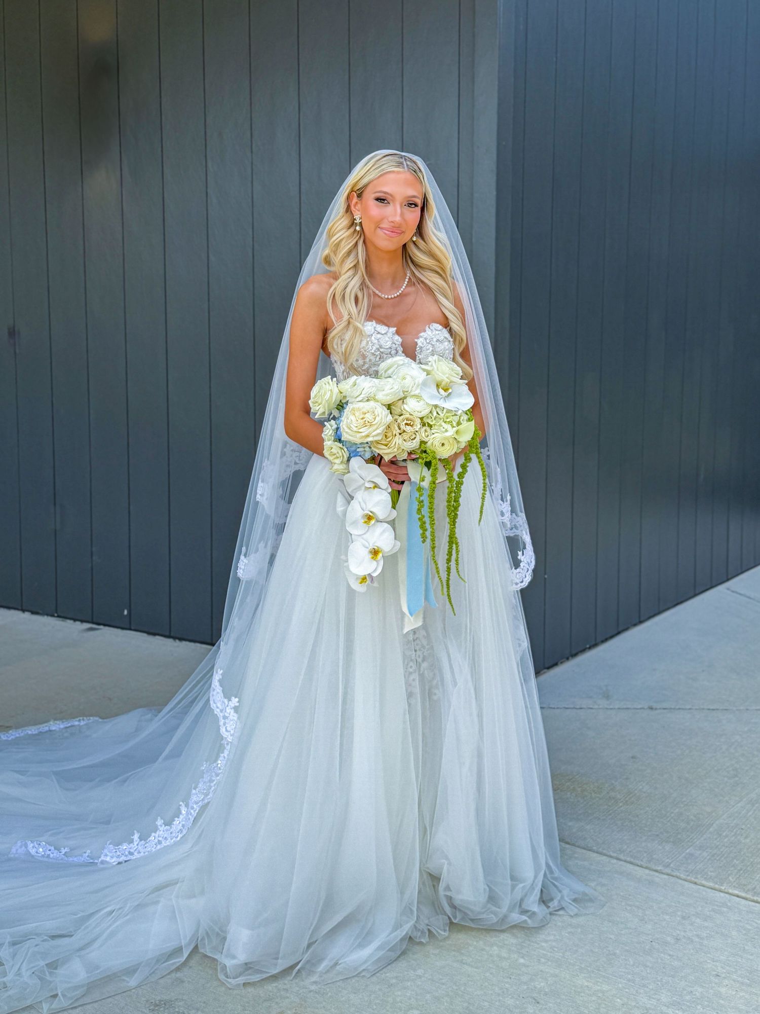 A white wedding dress with flowing train and cascading bouquet of white flowers.
