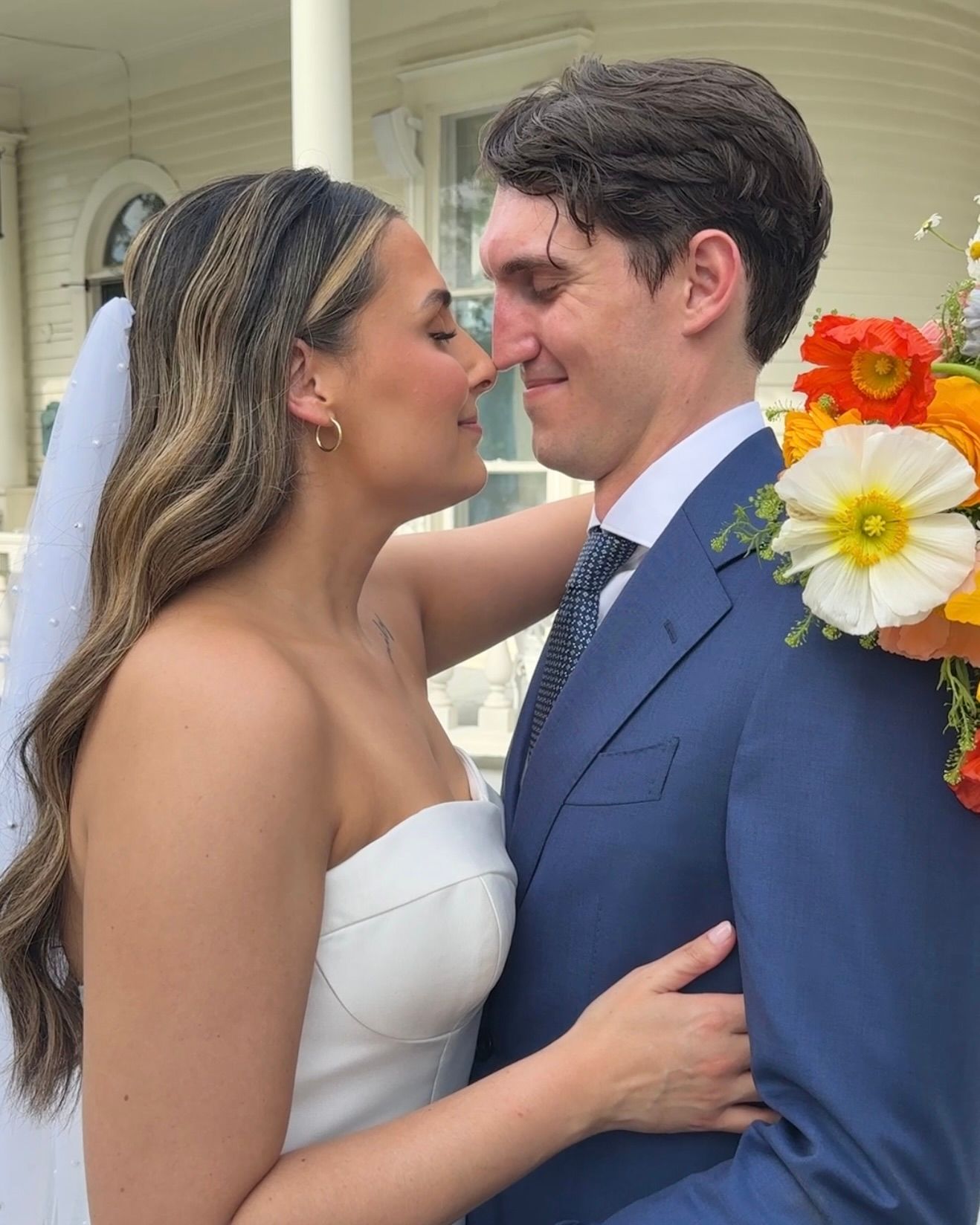 Romantic wedding couple shares intimate moments on a porch decorated with colorful flowers.
