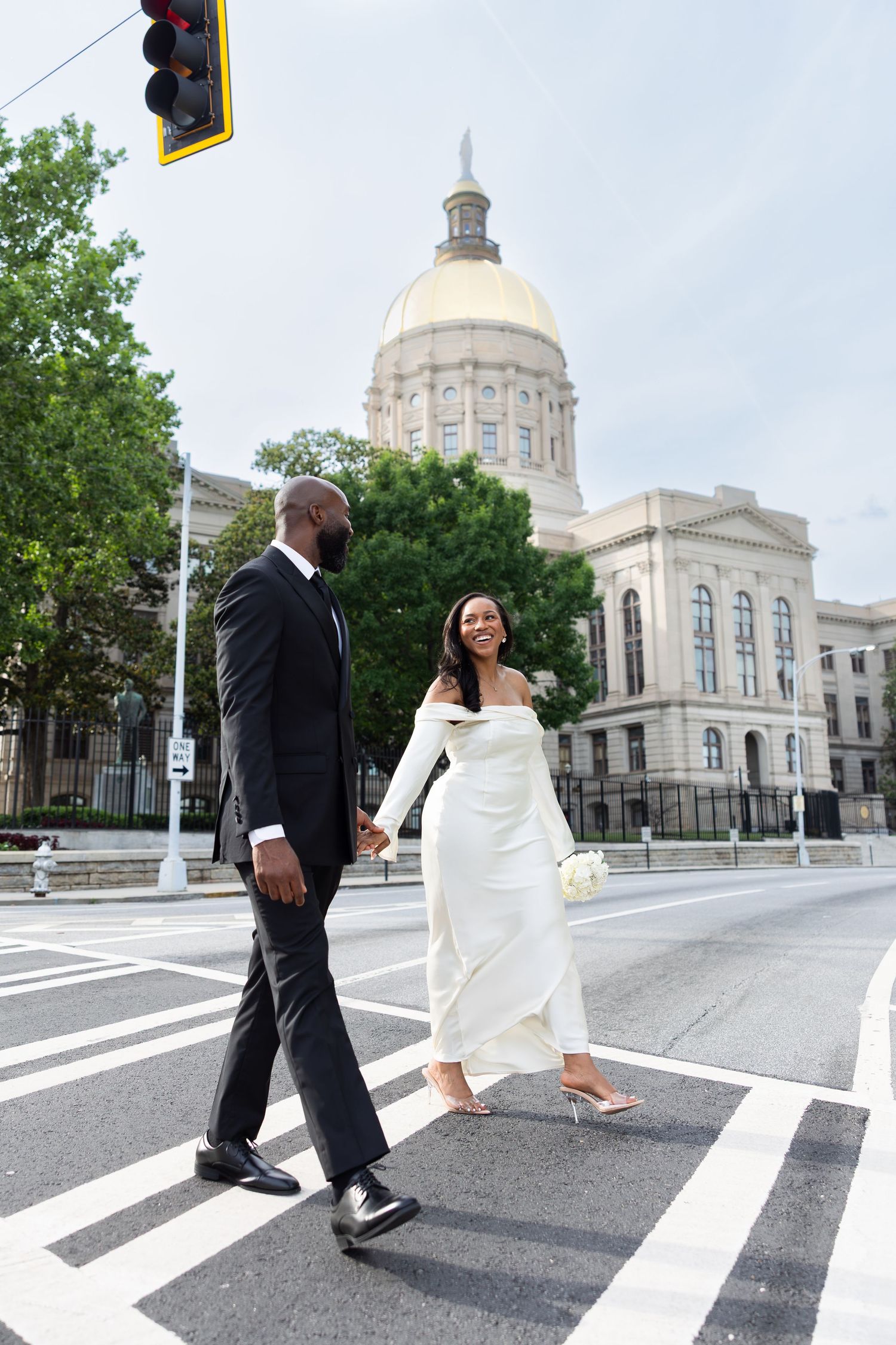Bride and groom crossing street in wedding attire near Georgia State Capitol building with gold dome.