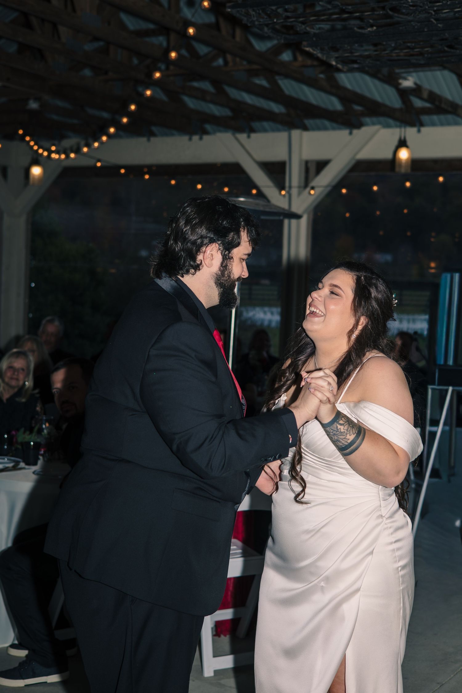 Couple shares intimate dance moments under string lights at indoor wedding reception venue.