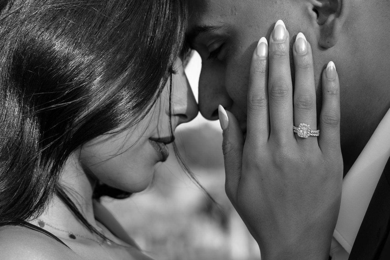 Black and white photo of a couple sharing an intimate moment, showcasing a stunning diamond engagement ring on her hand.