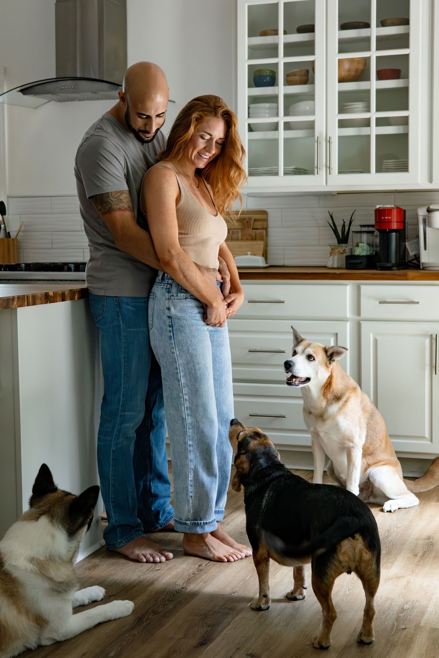 Couple dancing in their modern white kitchen while dogs watch curiously from the floor.