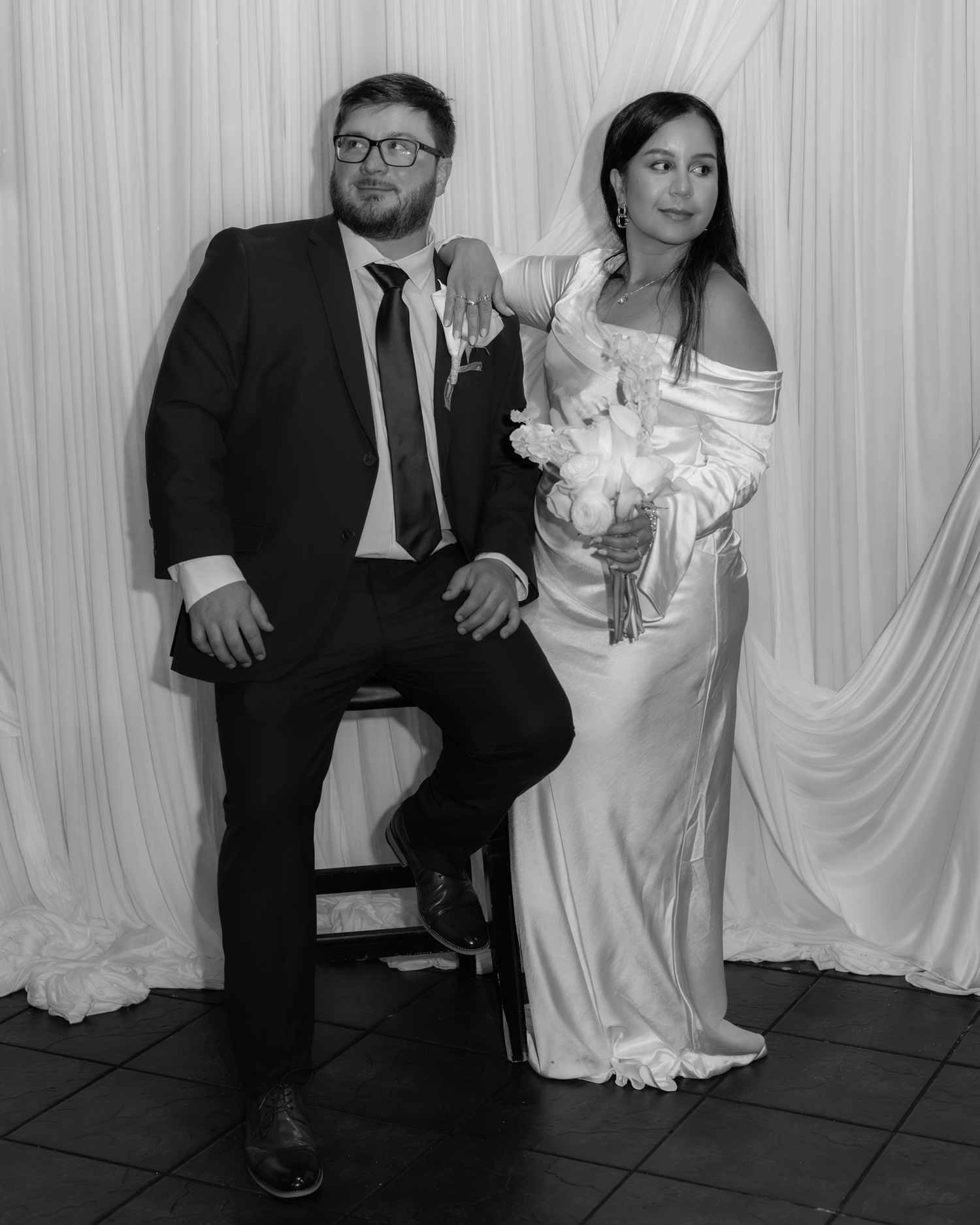 A man and a woman dressed formally stand together in front of a white backdrop.