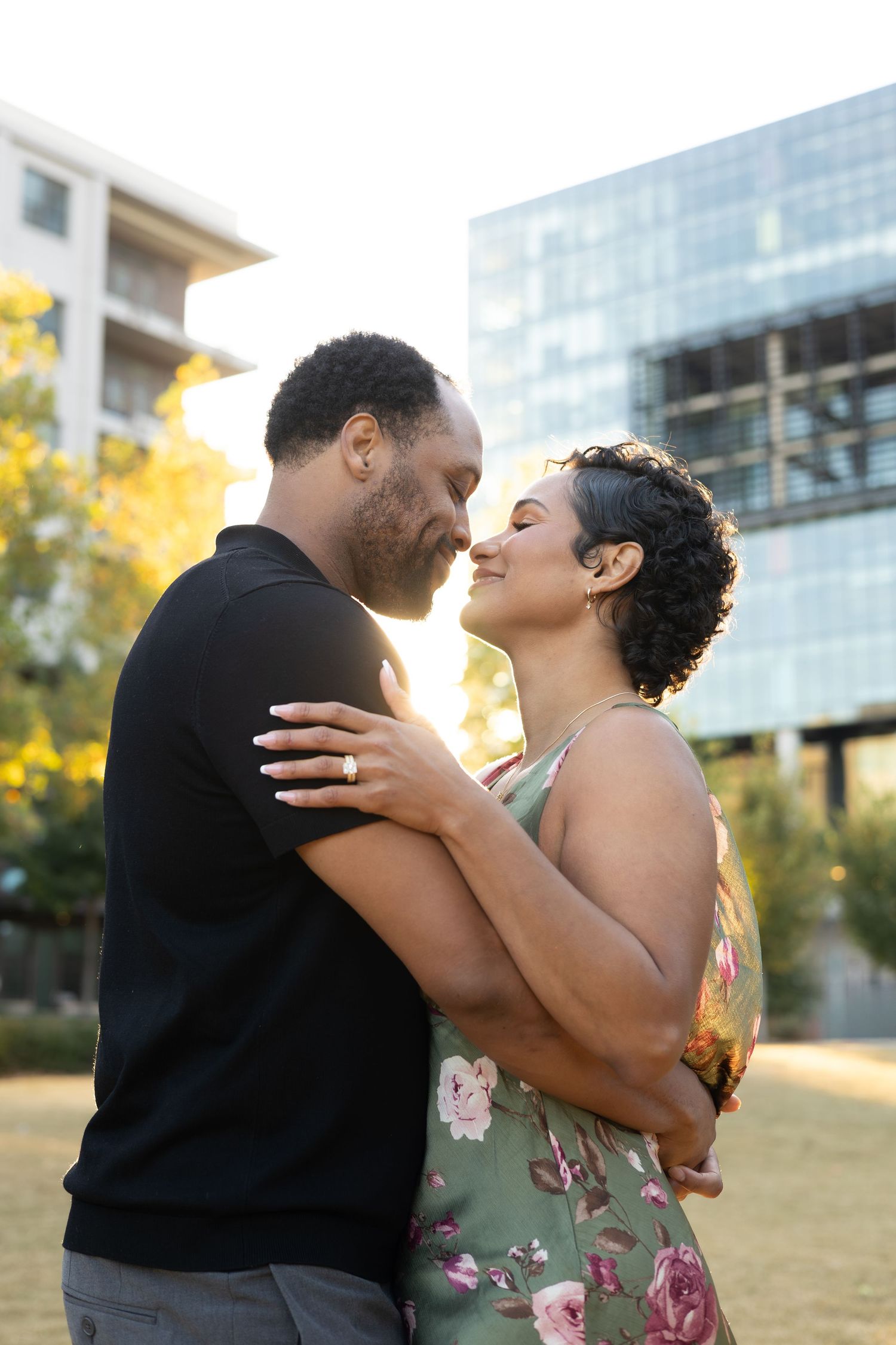 A romantic couple embraces and shares intimate moments outdoors near modern buildings.