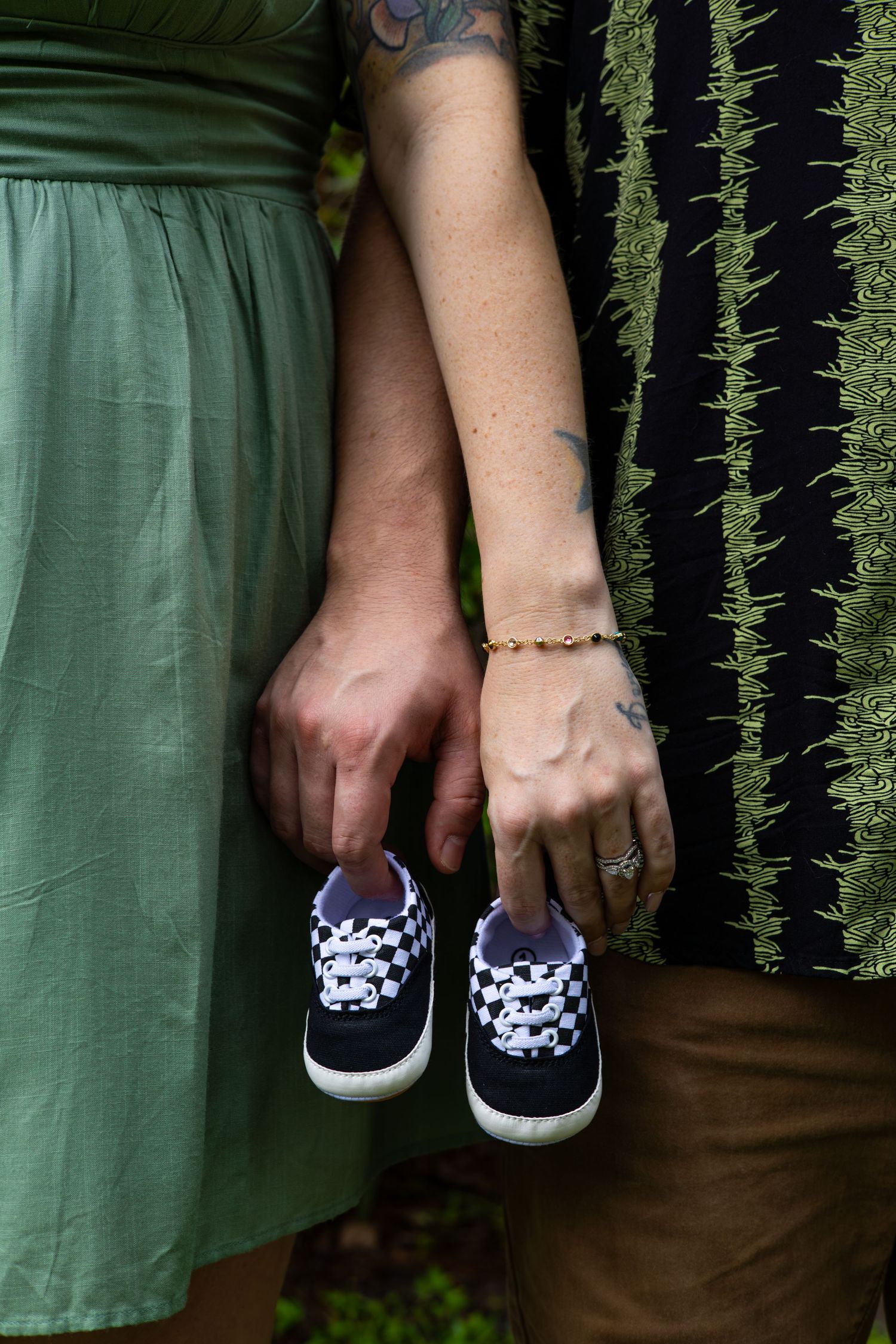 Hands holding tiny navy blue baby shoes against green and striped clothing.