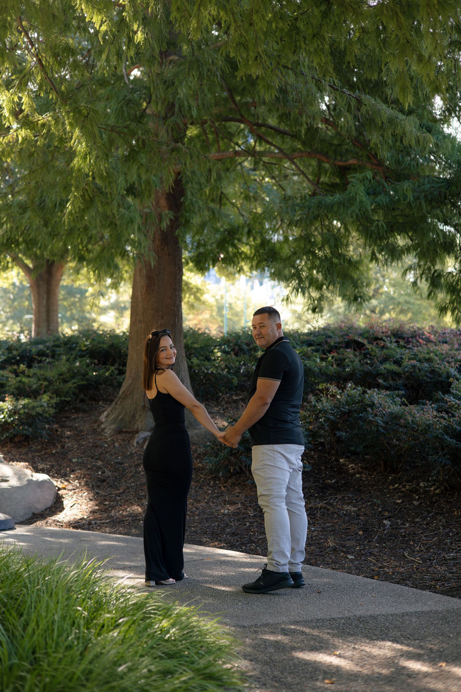 Couple sharing romantic moments on a tree-lined pathway in a park.