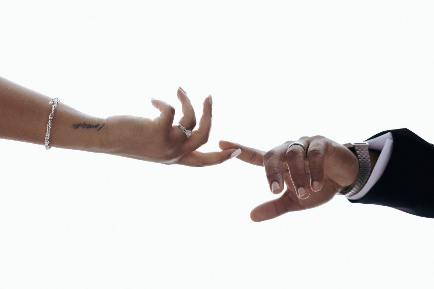 Two hands reaching towards each other against a white background, one wearing a formal suit sleeve and one with a bracelet.