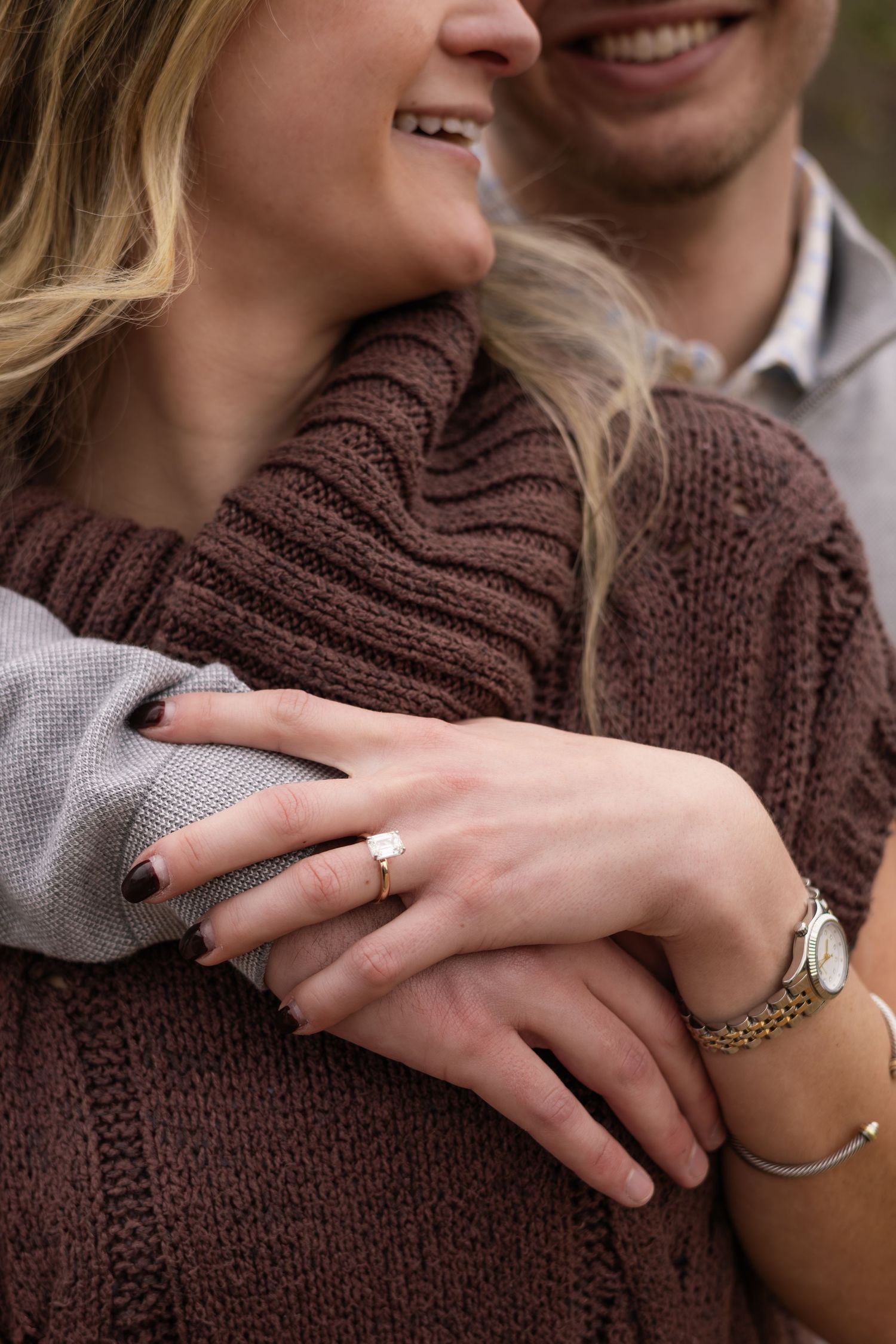 Close-up shot showing hands embracing with engagement ring and jewelry details.