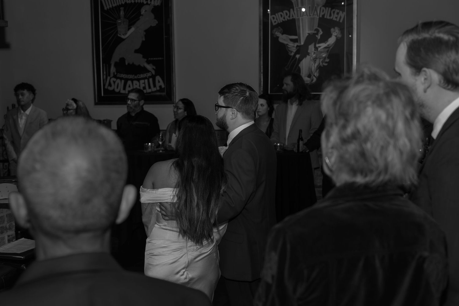 Black and white candid shot of wedding guests mingling at a reception venue.