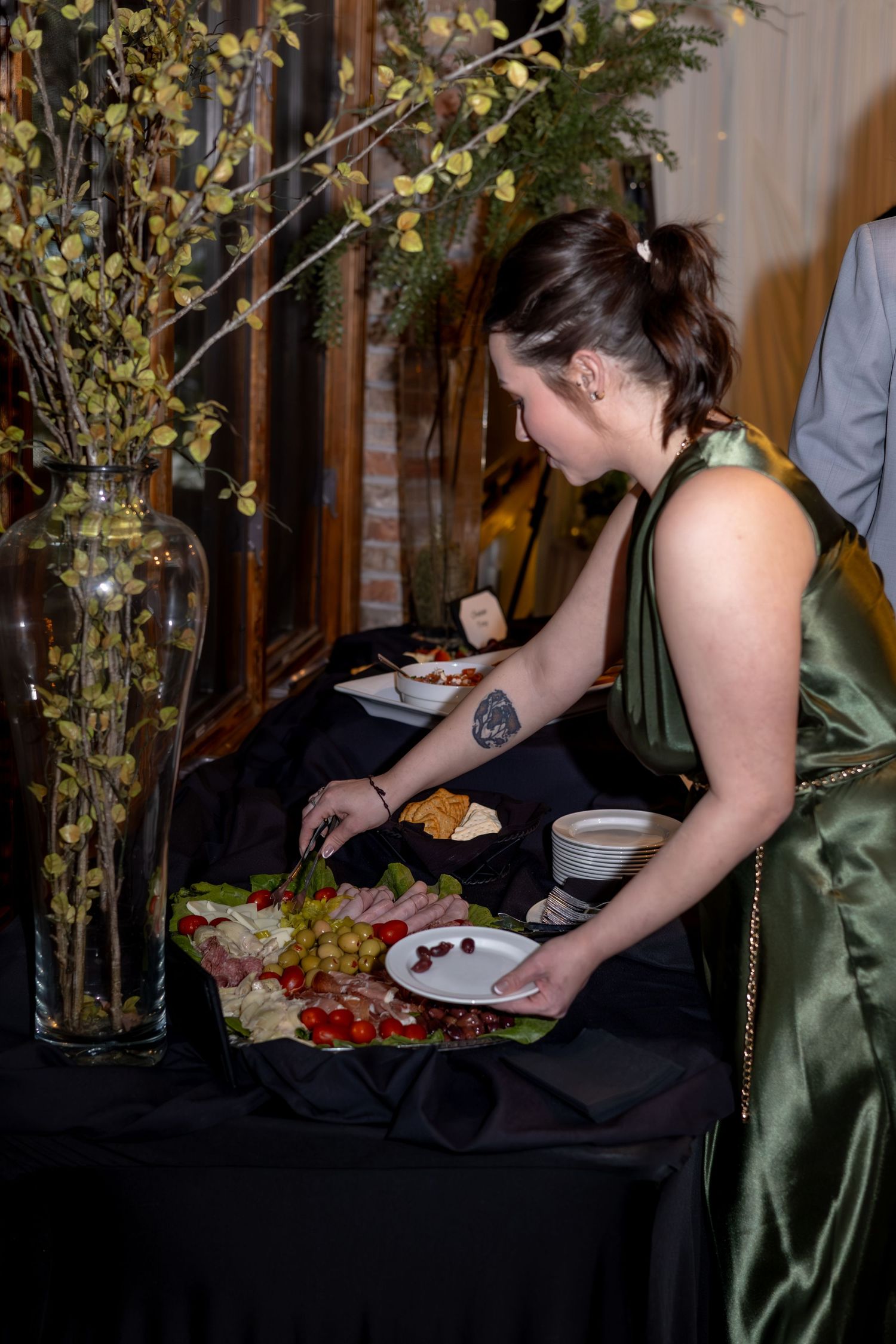 The image shows a woman in a green dress sitting at a table with various food items, including grapes, in front of a vase of flowers.