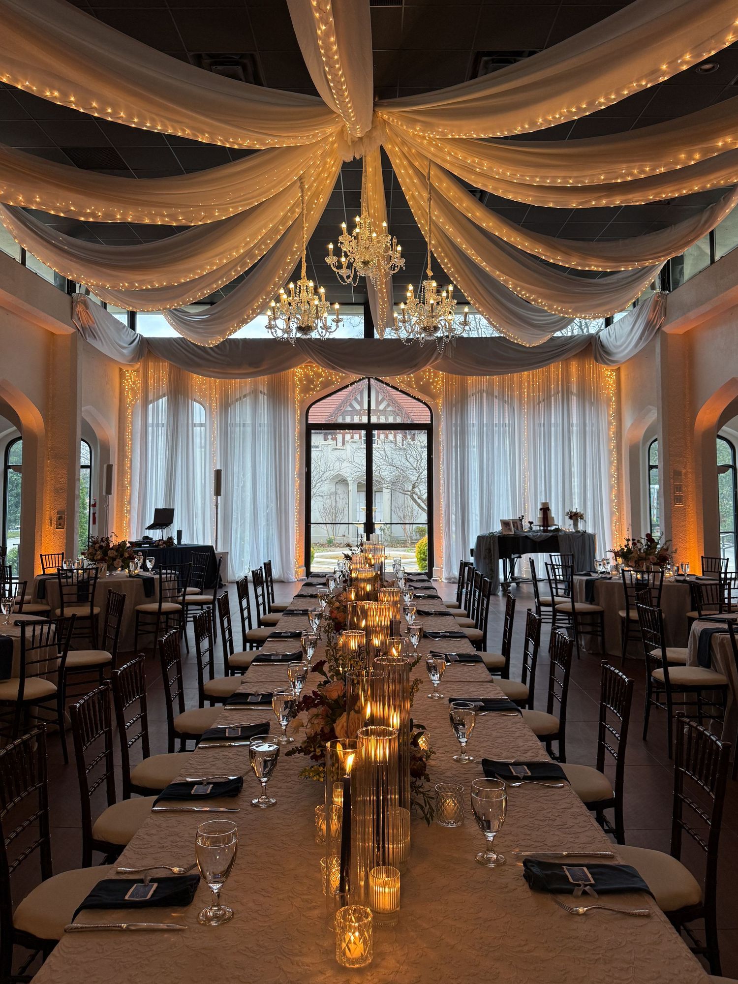 Elegant wedding reception venue with draped fabric ceiling, chandeliers and intimate table settings.