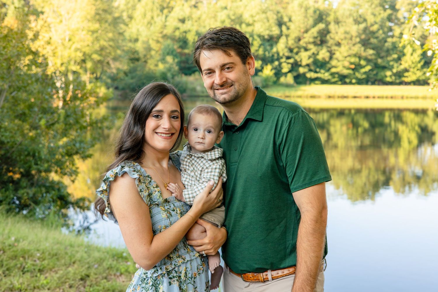 A happy family of three, a mother, father, and young child, enjoying a peaceful moment by a lake surrounded by nature.
