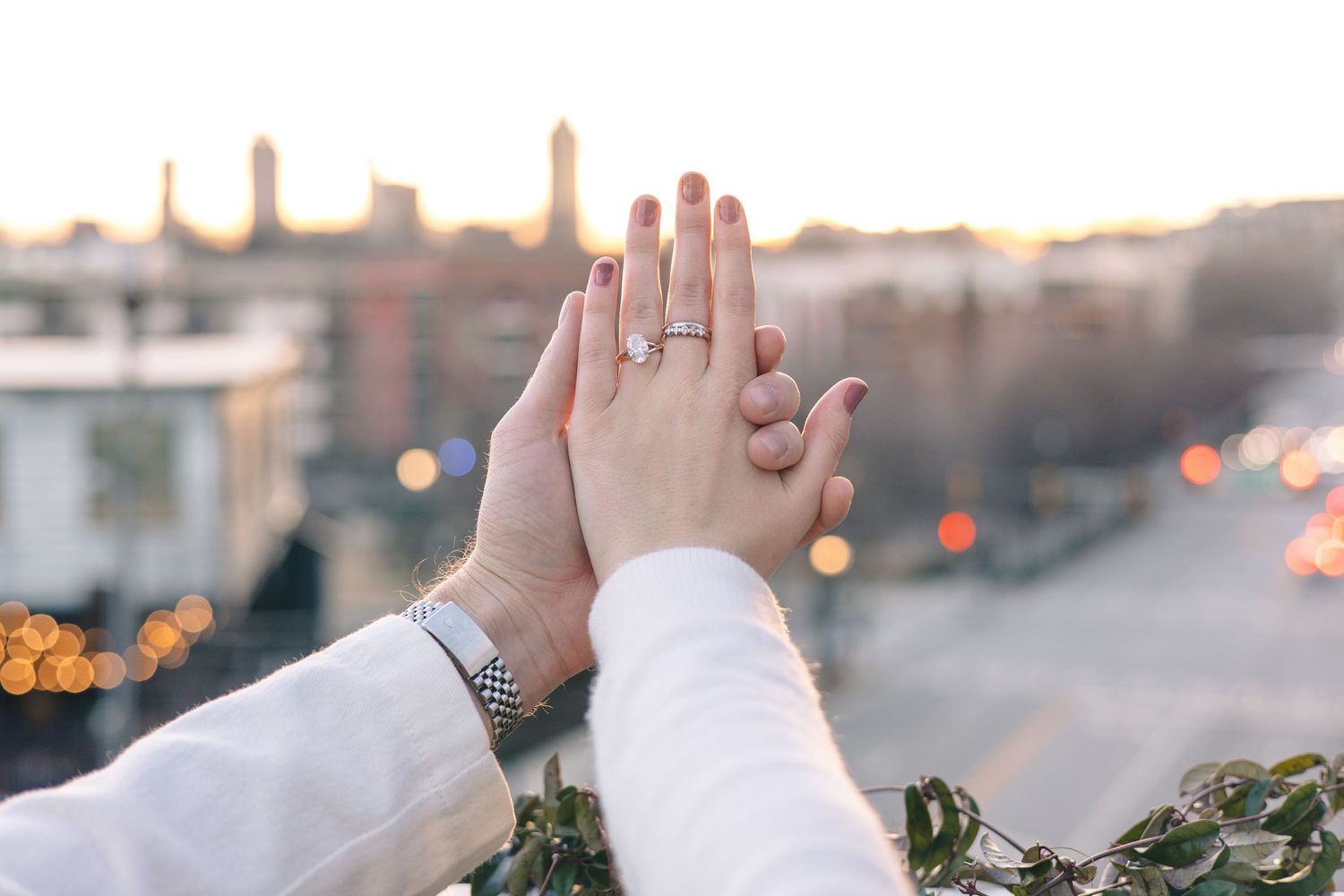 Close-up of hands raised against sunset sky with city lights in background.