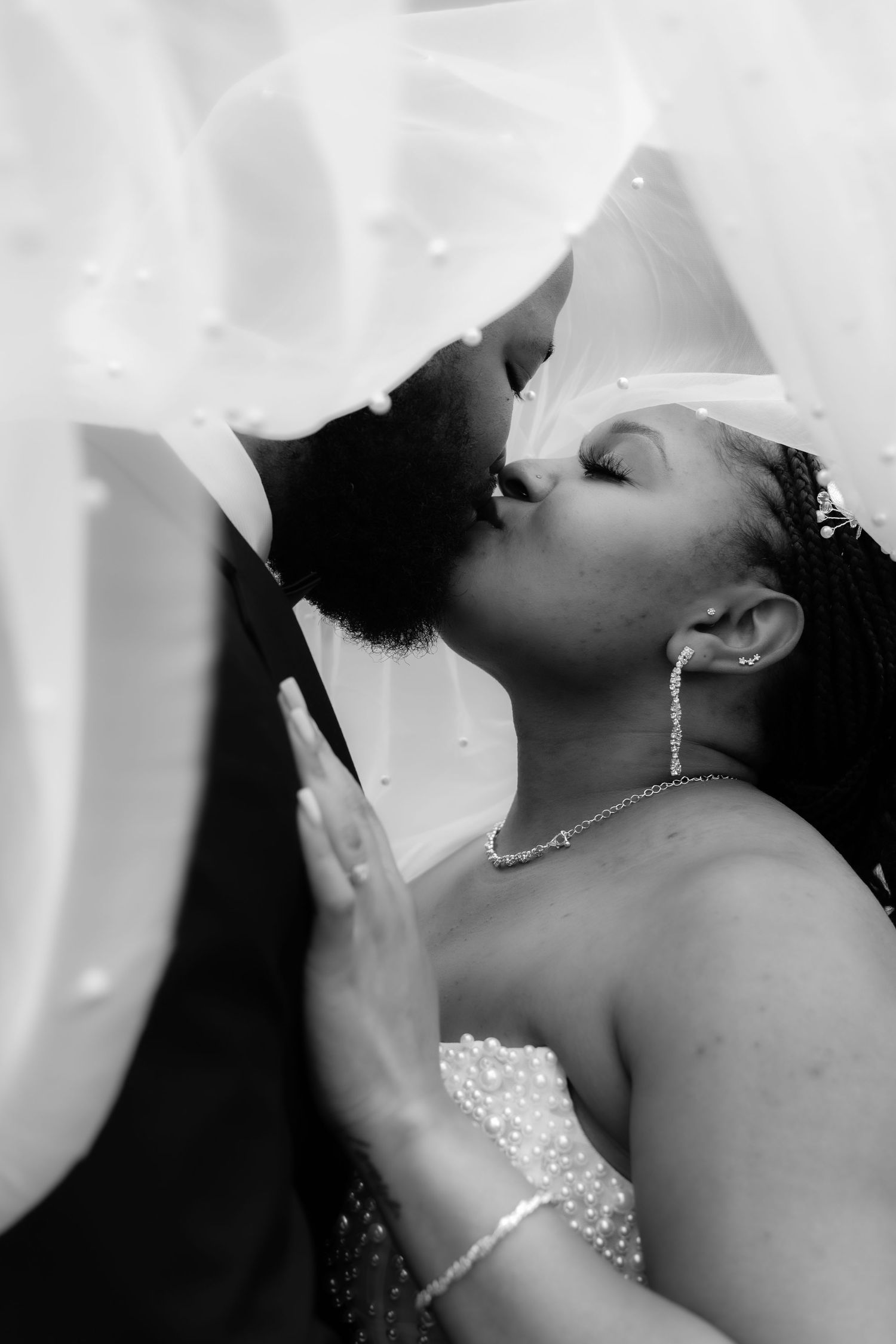 A romantic black and white wedding photo showing a tender kiss between a couple, with the bride wearing a sparkly dress.