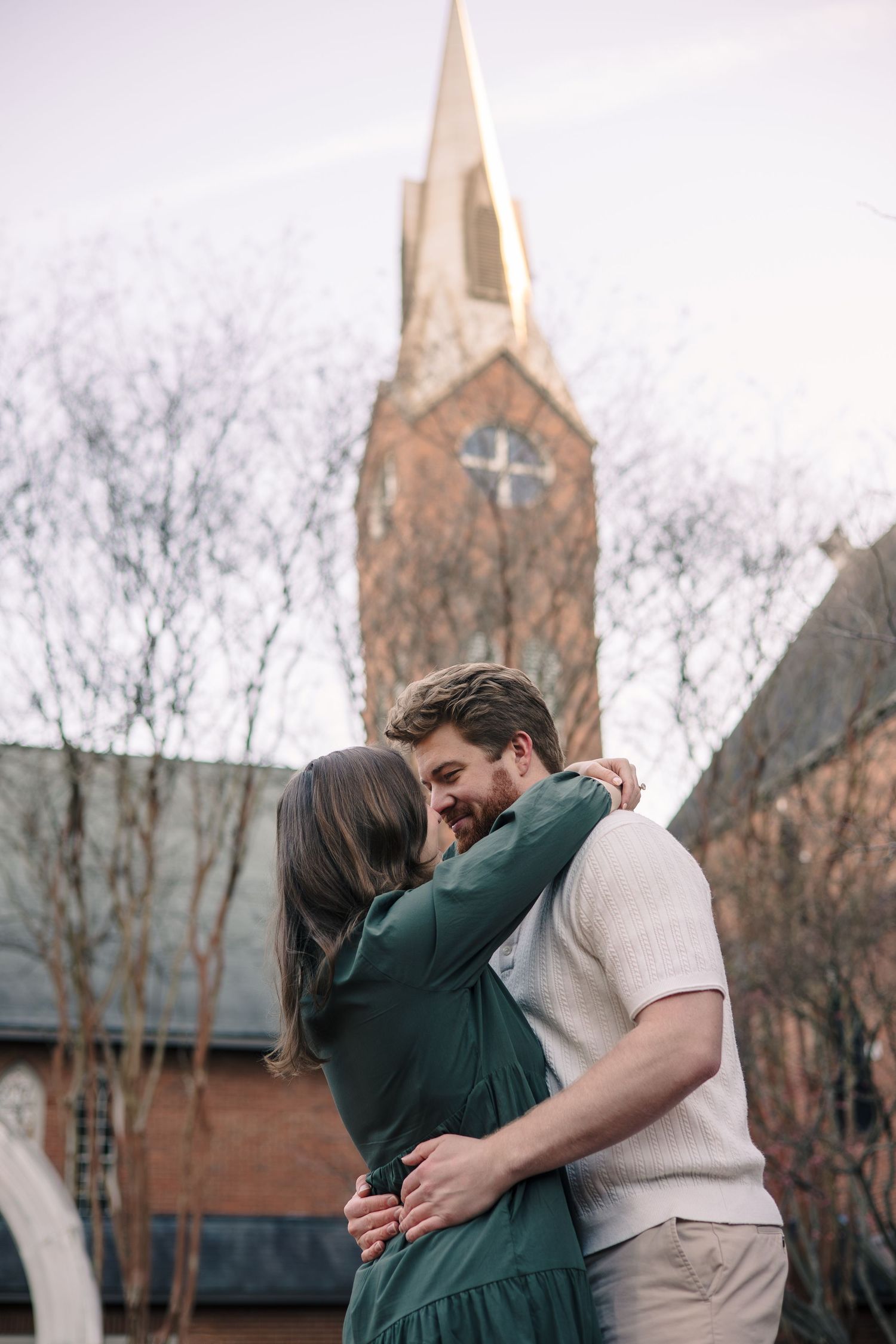 A romantic embrace in front of a brick church with a tall spire.