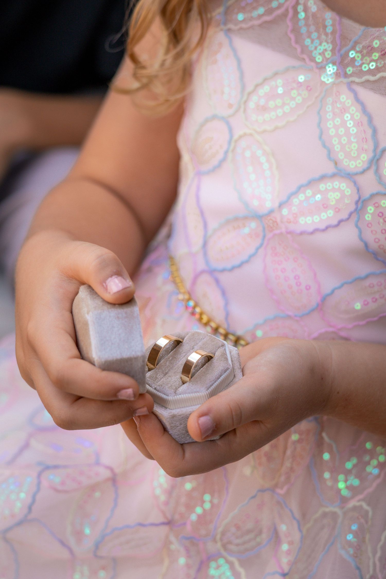 Close-up of hands holding a small ring box with sparkly dress fabric in the background.