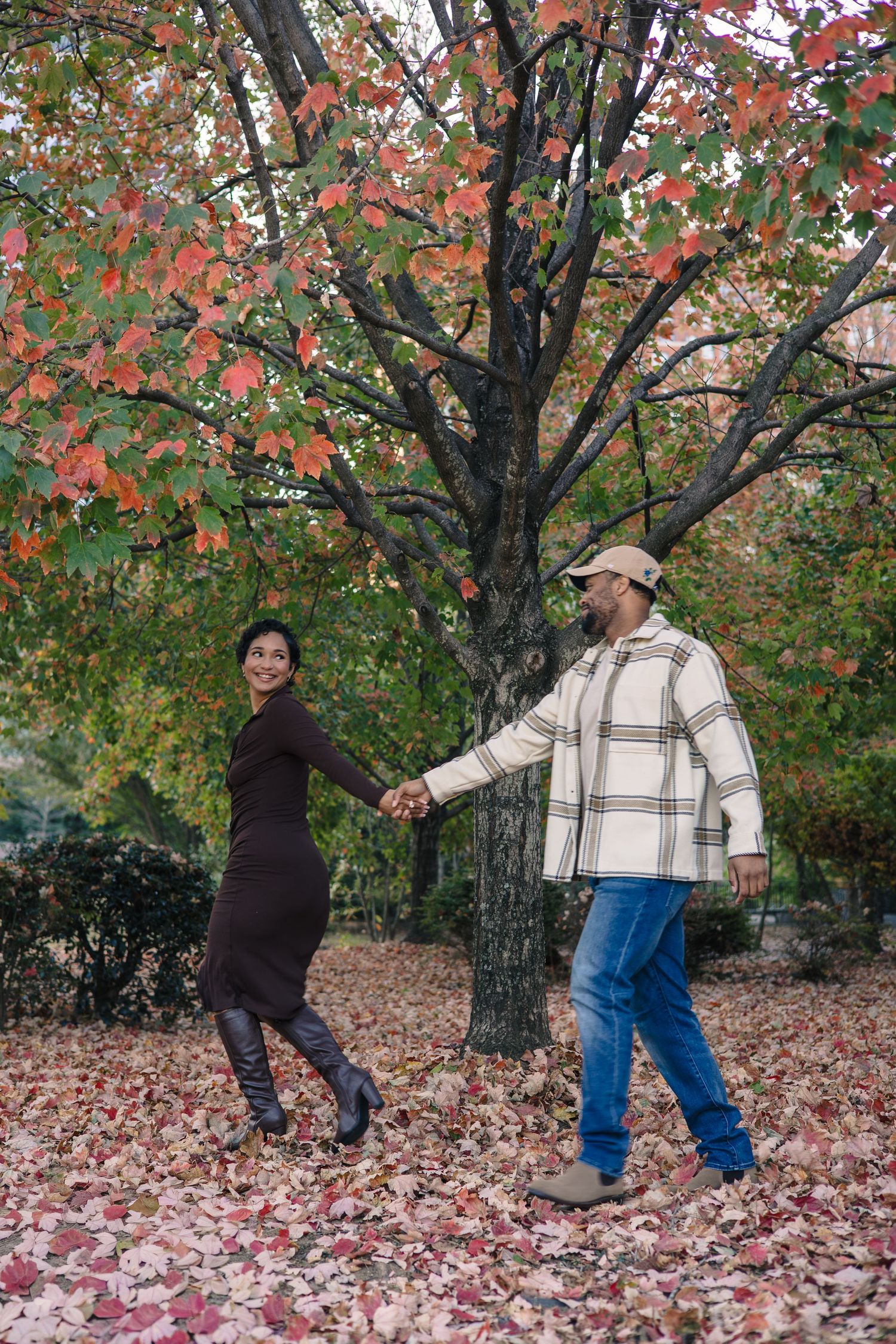 Two people play and dance together in a park filled with colorful fall foliage.