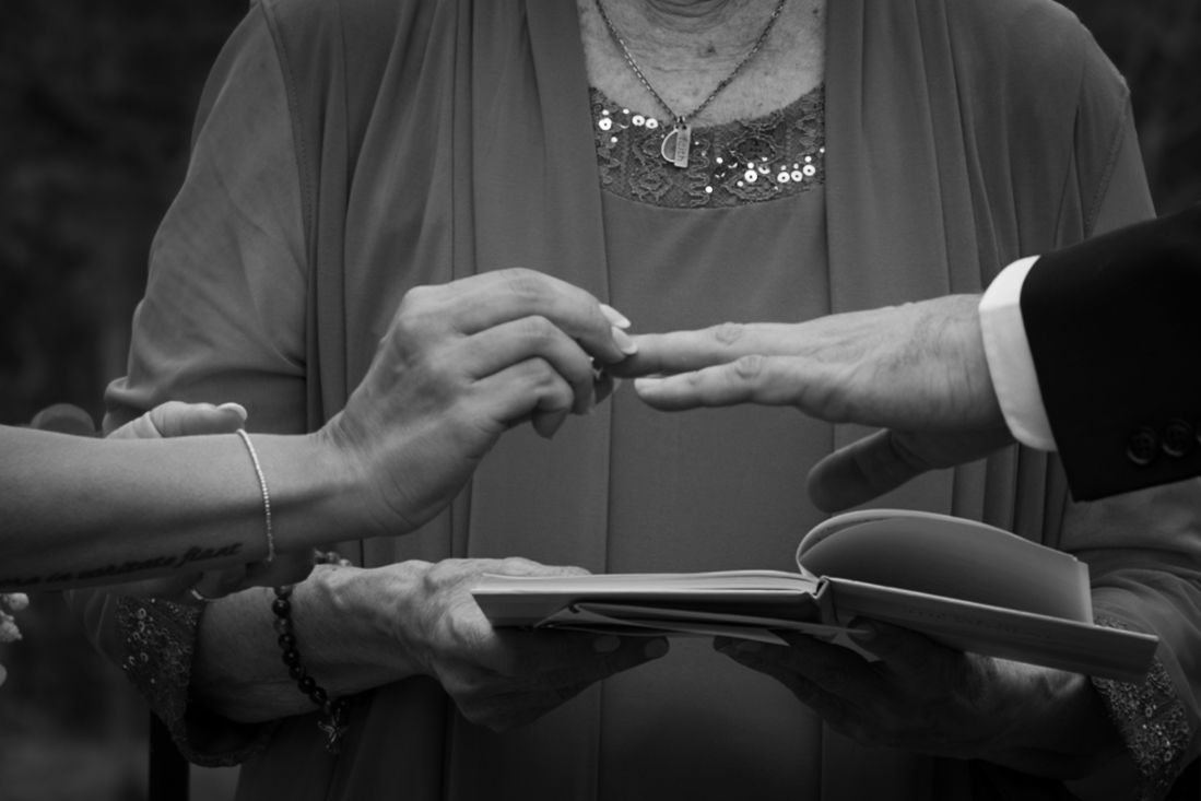 Black and white image of hands exchanging rings during a wedding ceremony.