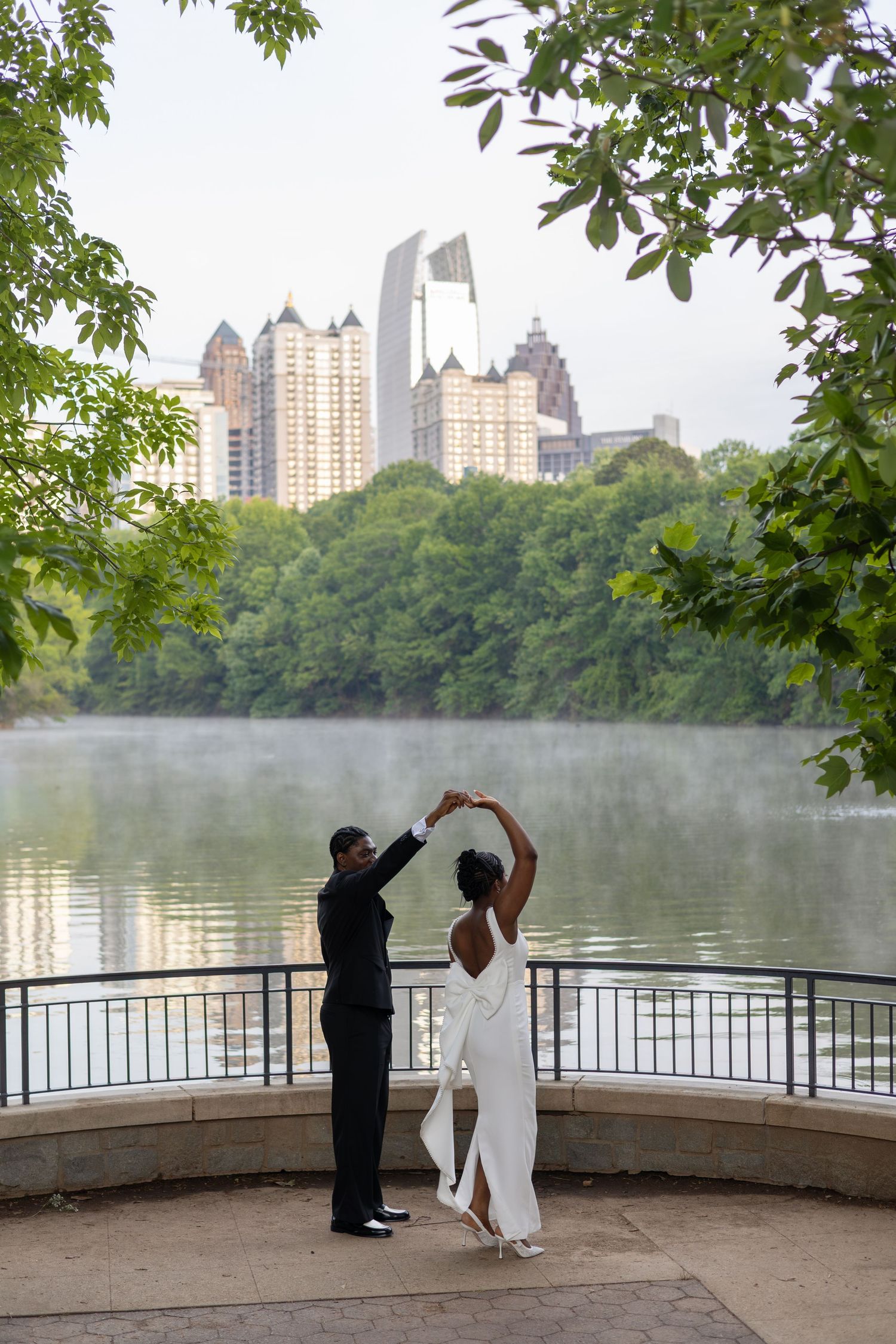 Couple dancing elegantly by a misty lake with Atlanta city skyline and lush green trees in the background.