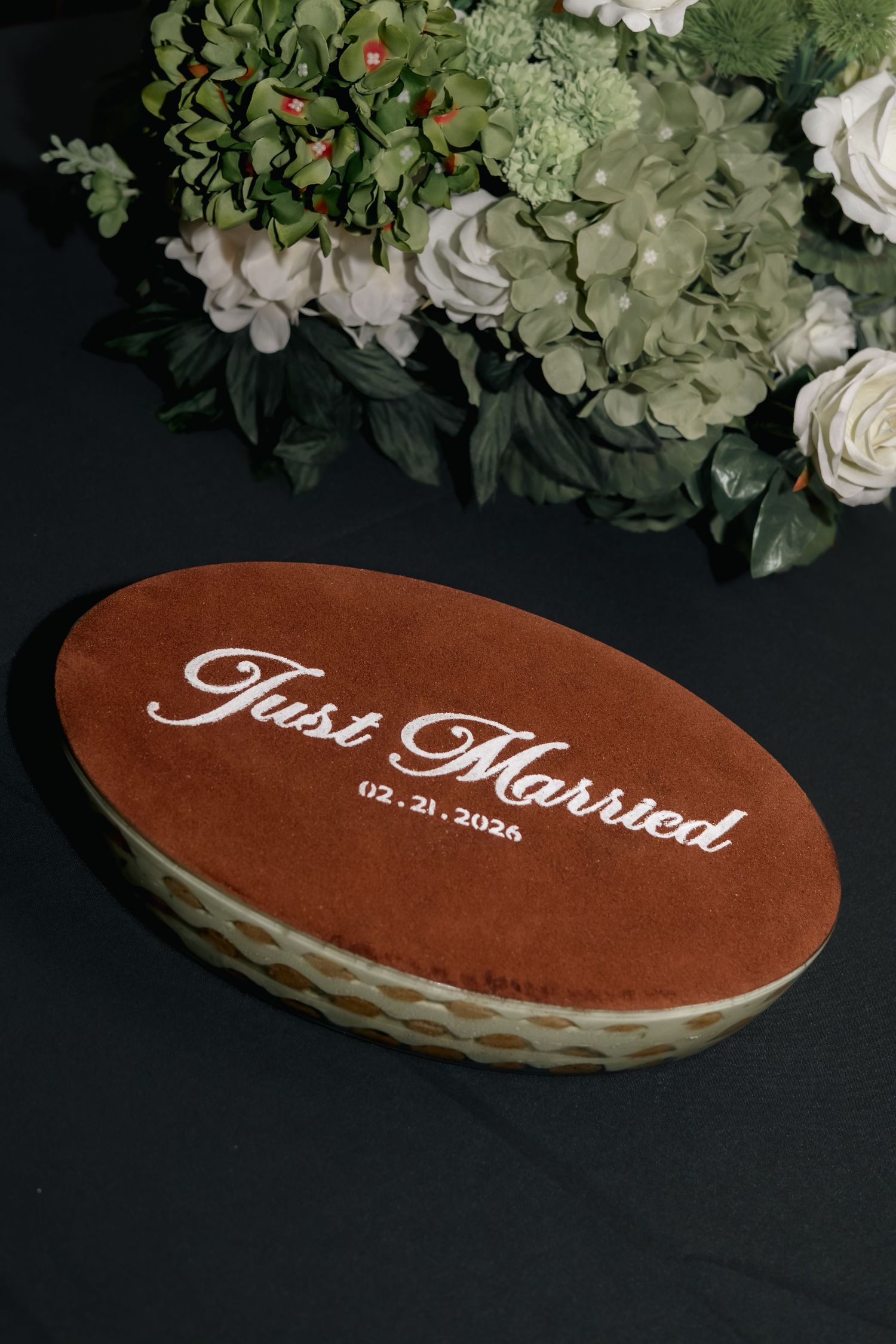 Brown velvet wedding sign reading 'Just Married' with white roses and greenery arrangement.